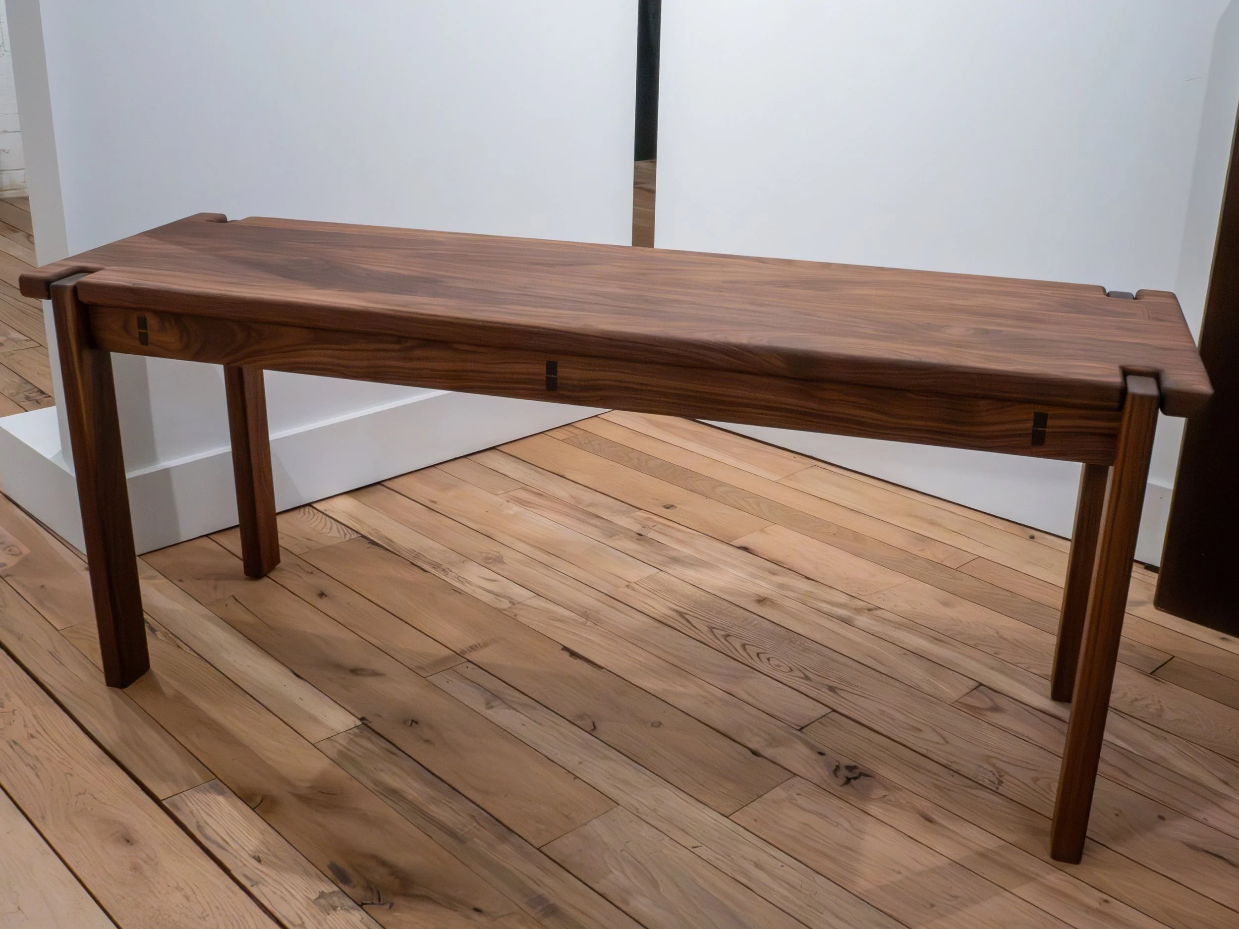 A wooden console table with a sleek, minimalist design placed on a wooden floor in an indoor setting.