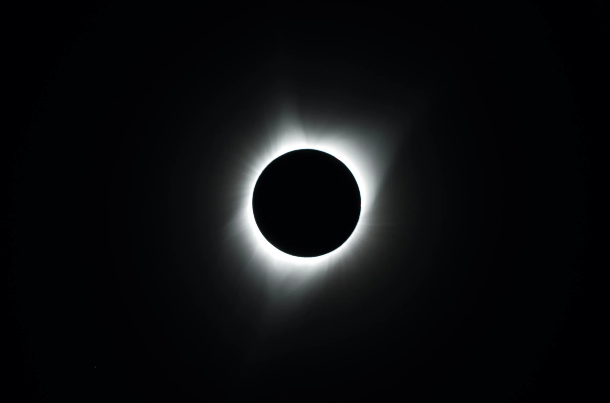 A solar eclipse where the moon is covering the sun, creating a dark circle with a bright white corona around it.