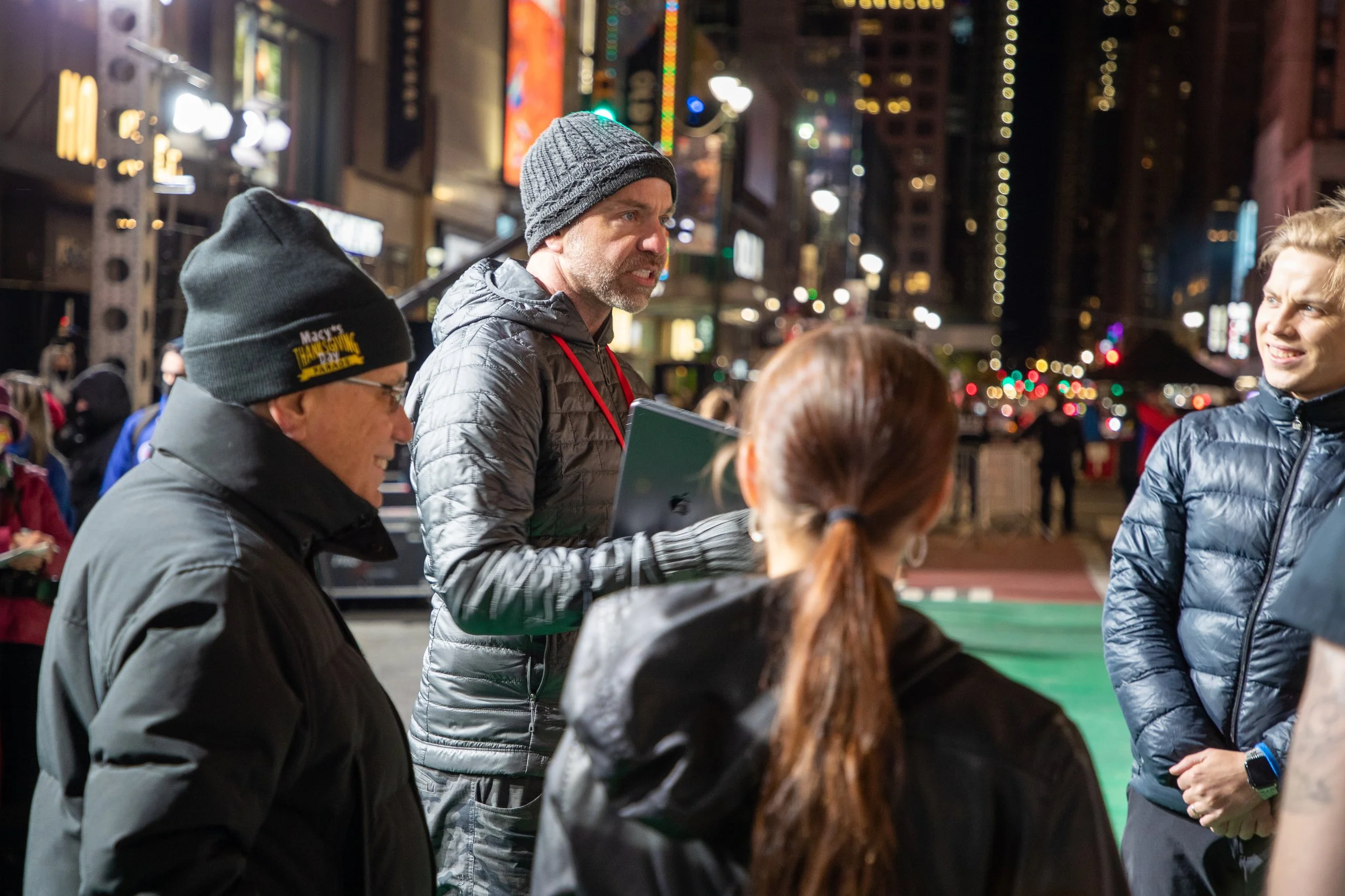 Group of people wearing warm clothing talking outdoors in a city at night, possibly preparing for an event.
