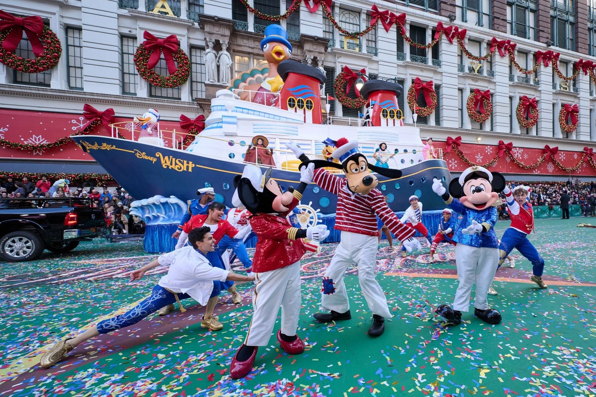 Disney parade float featuring a large ship with characters, dancers in festive costumes, and confetti.