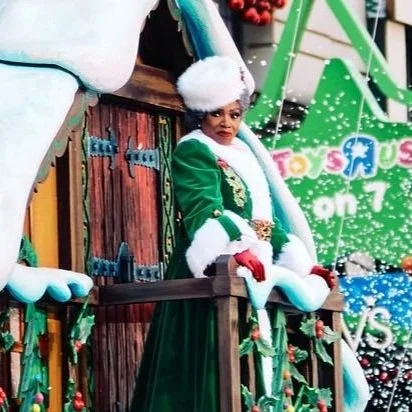 Sheryl Lee Ralph dressed as Mrs. Claus in festive attire on a holiday parade float with decorations.