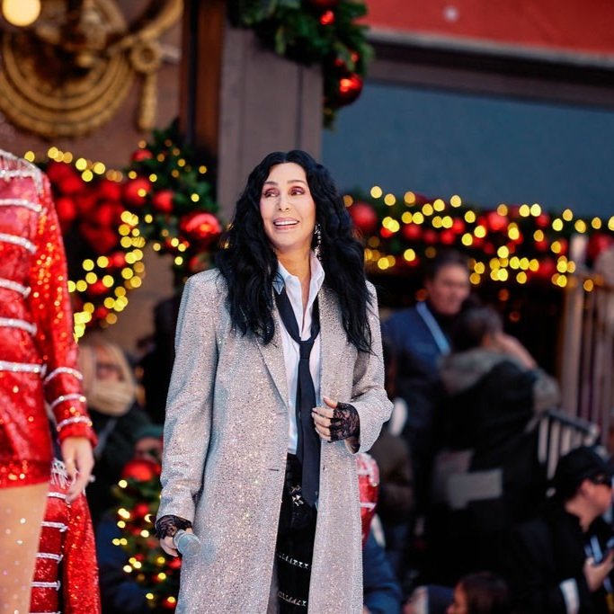 Cher wearing a festive outfit with Christmas decorations in the background.