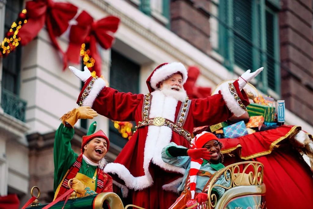 Santa Claus in a parade with elves on a festive float.
