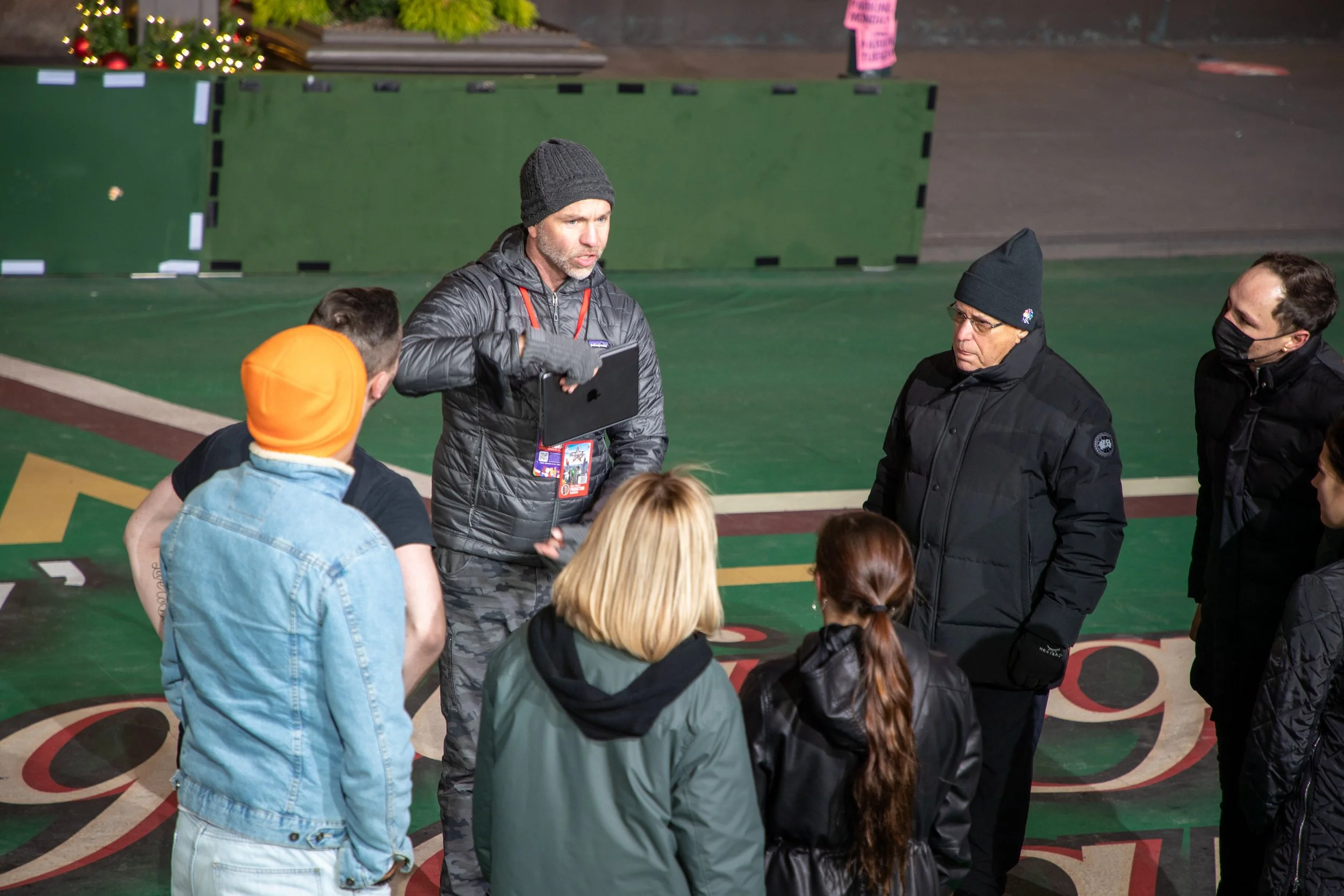 Group of people having a discussion outdoors at night, standing on a colorfully painted surface, wearing winter clothing including hats and jackets.