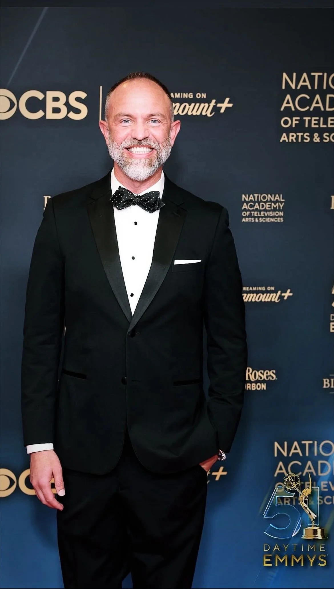 A man in a tuxedo at a Daytime Emmys event, against a backdrop with logos of CBS, Paramount+, and the National Academy of Television Arts & Sciences.