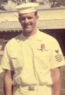 Young man in US Navy uniform standing outdoors.