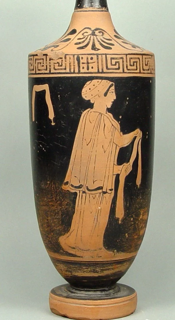 Ancient Greek vase depicting a standing woman wearing a draped dress and a head covering, holding a cloth or garment, with decorative patterns near the neck and top.