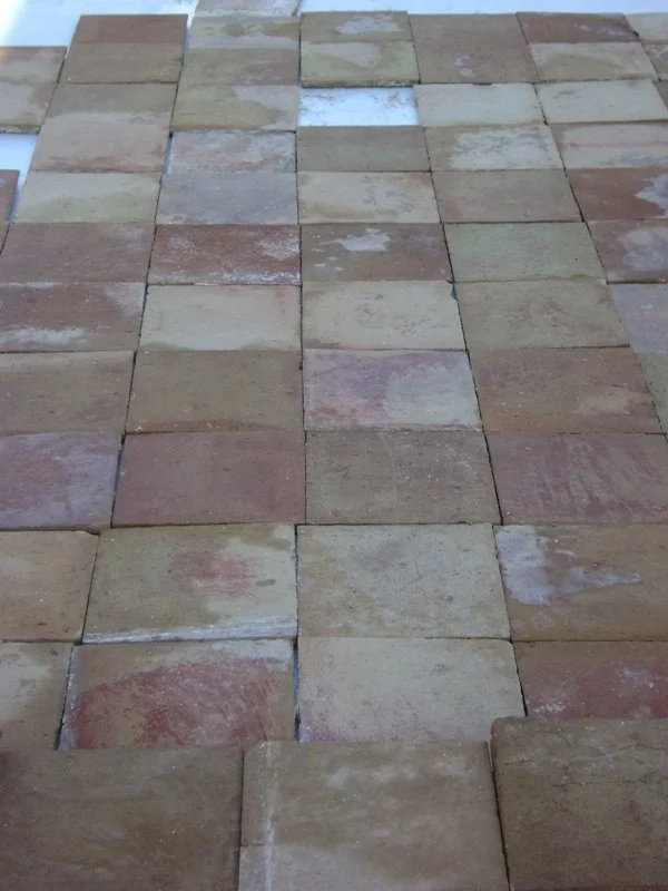 A close-up view of a paved brick pathway with various beige, brown, and pinkish stones arranged in a rectangular pattern.