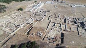 Ancient archaeological ruins with stone foundations and structures, viewed from above in a desert-like area.