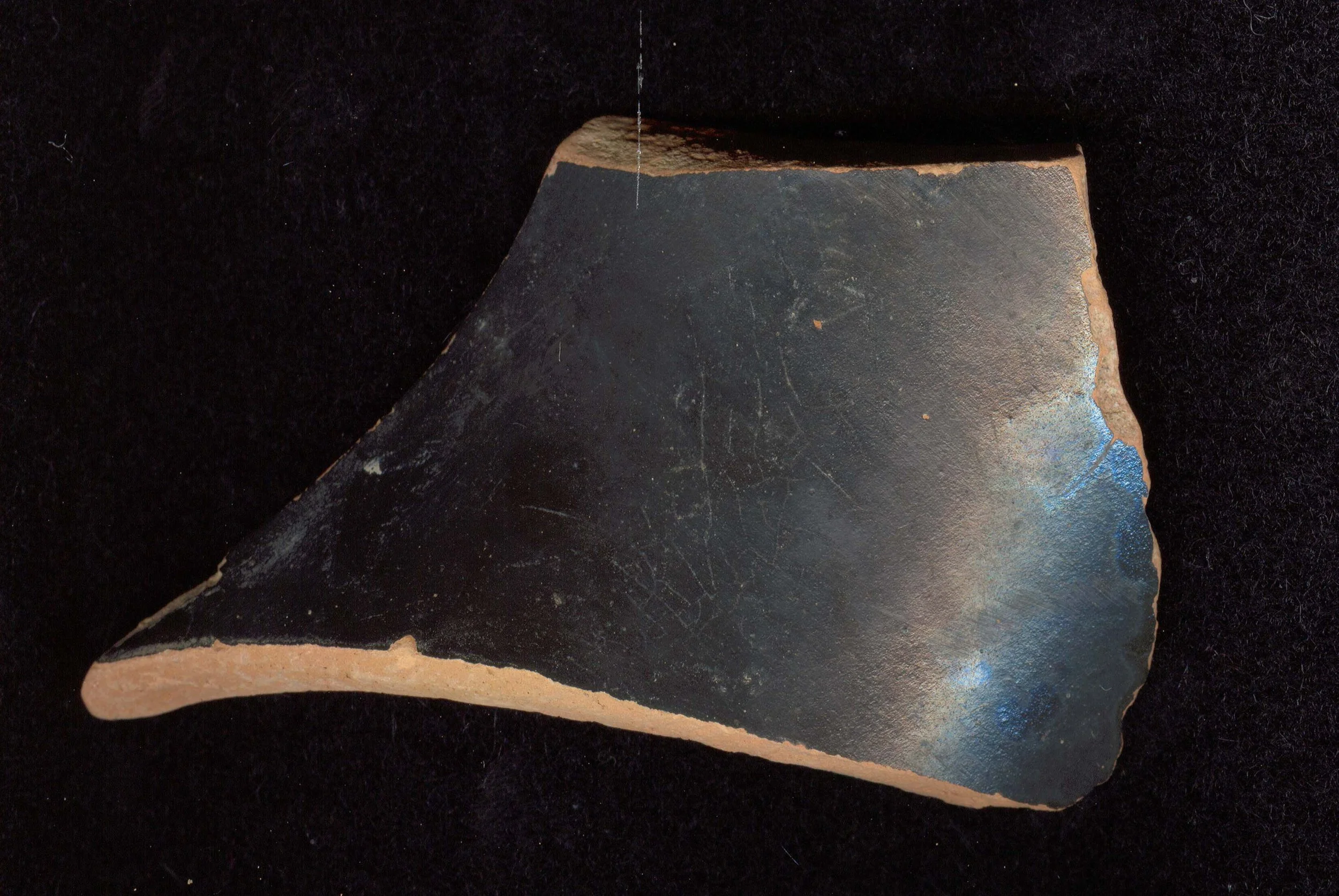 A piece of a broken black and orange ceramic object resting on a white measured device with warning labels about high radiation levels, against a background of beige wall and a wooden panel.