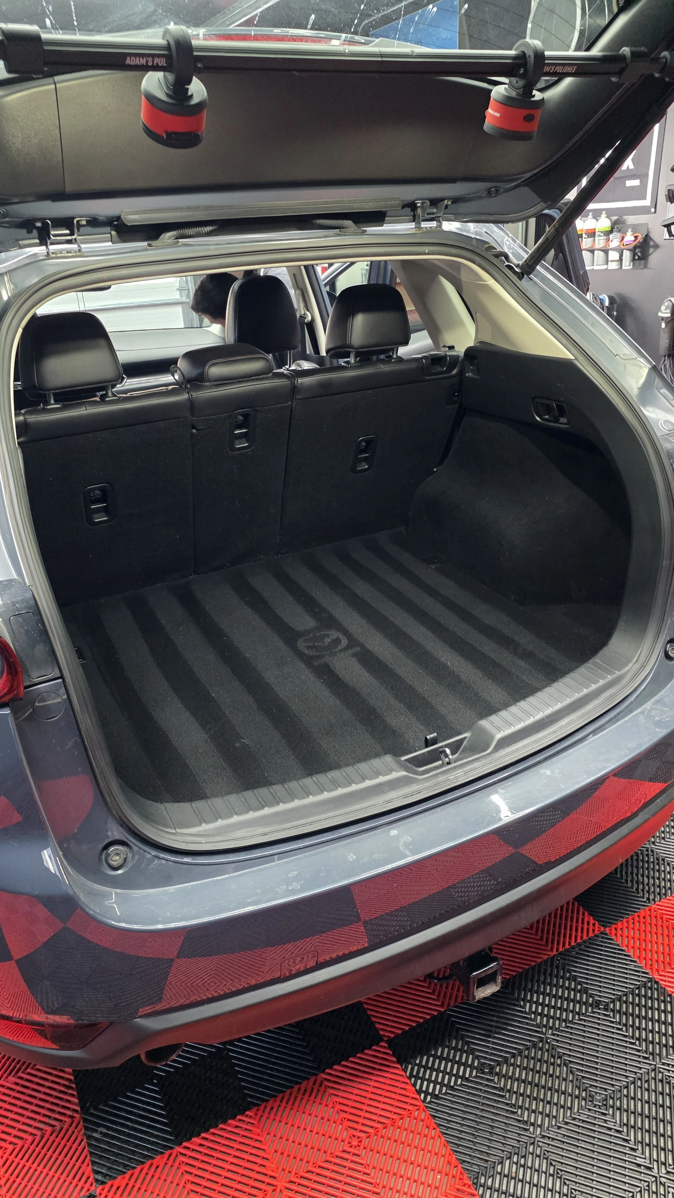 Open trunk of a silver SUV showing a black carpeted cargo area with rear seats, with a person partially visible inside the vehicle.