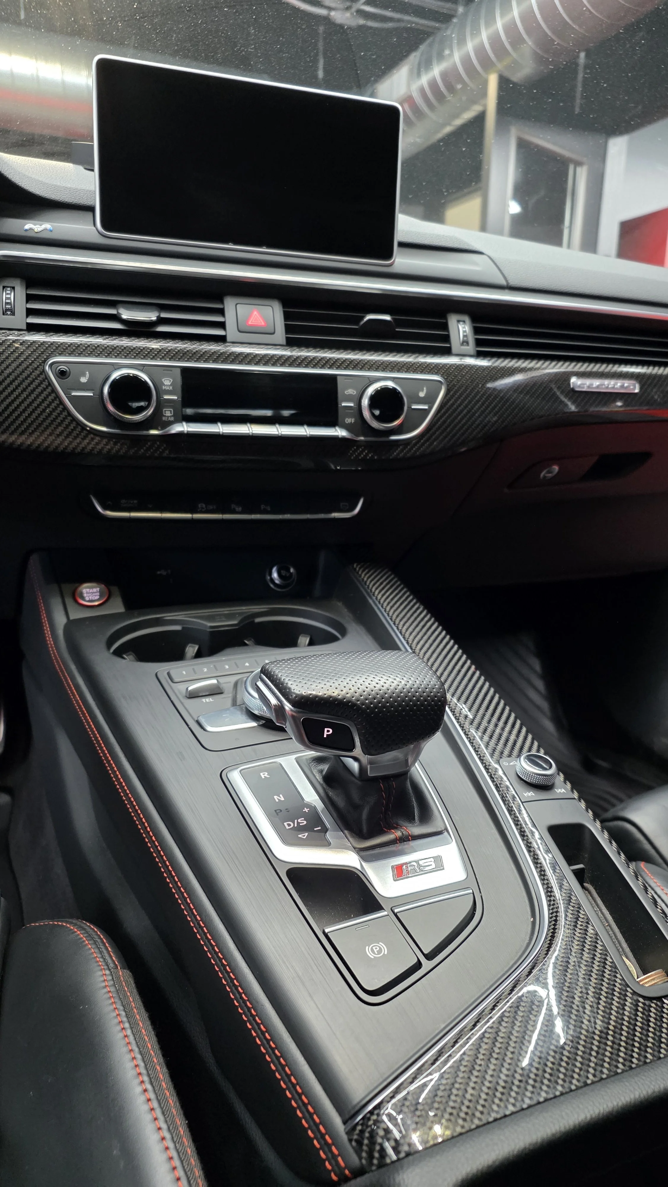 Interior of a car showing a dashboard with a display screen, climate controls, and a gear shift with an 'RS' badge.