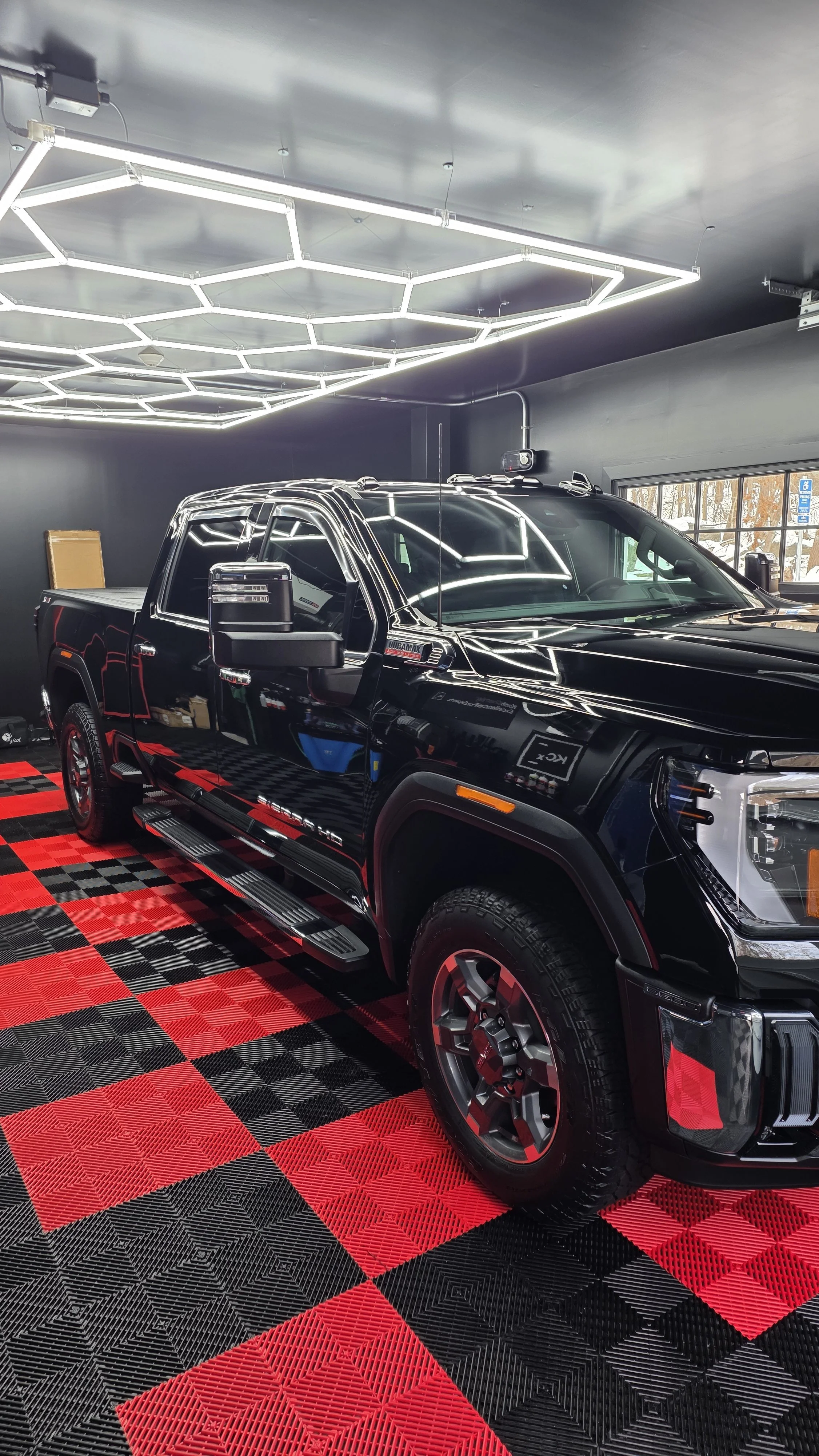 A black pickup truck with chrome accents parked inside a modern showroom with black walls and a illuminated hexagonal ceiling light fixture. The showroom features a red and black checkered floor.