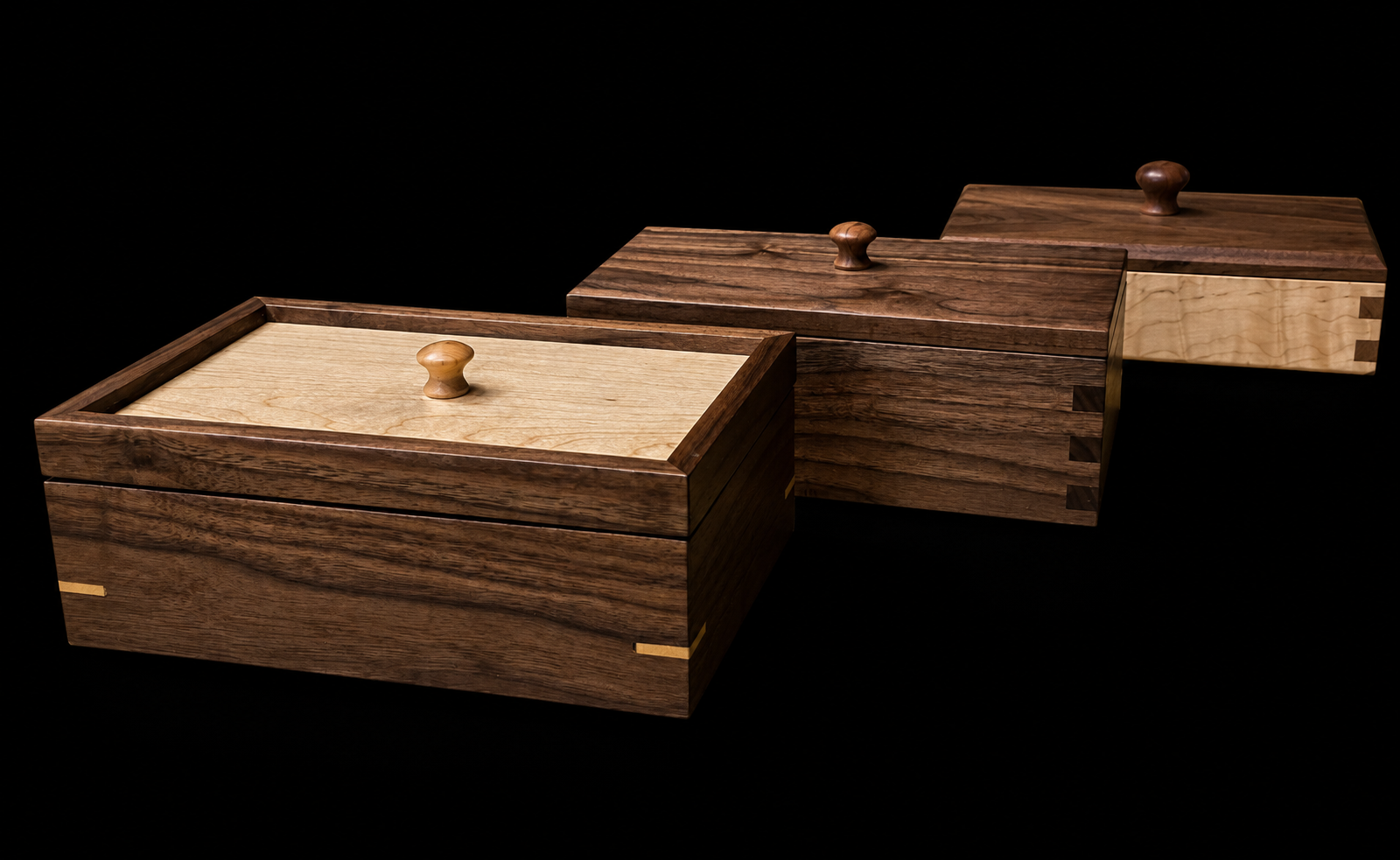 Three wooden boxes with lids, made from different types of wood, arranged against a black background.
