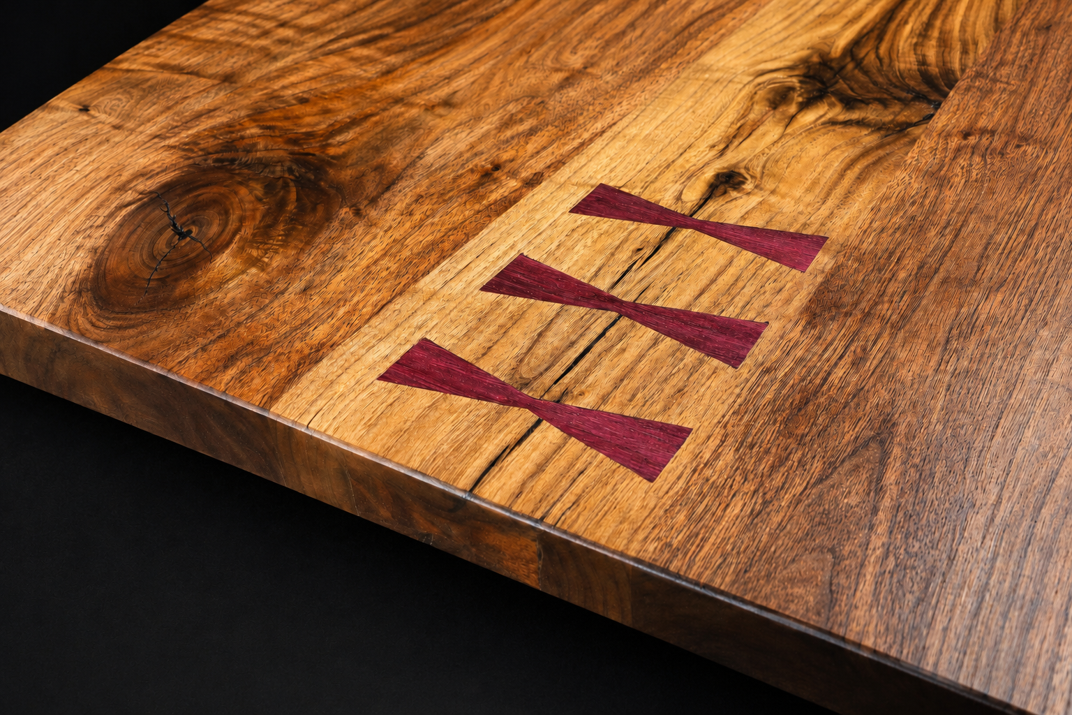 Close-up of a rustic wooden cutting board with three maroon-colored wooden wedges embedded in the surface.