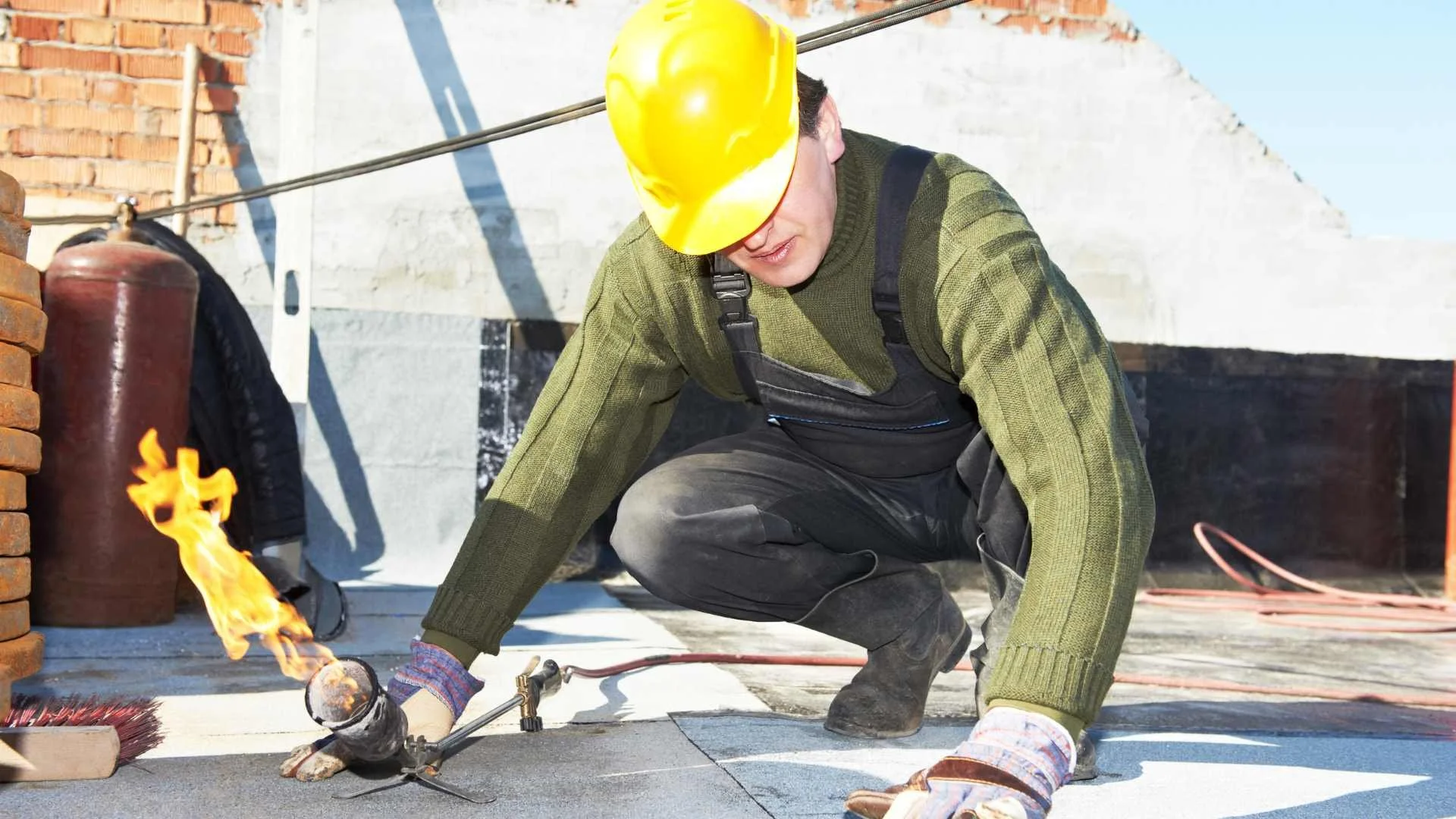 one of commercial roofing mobile al's roofer in a yellow hard hat working on a flat roof