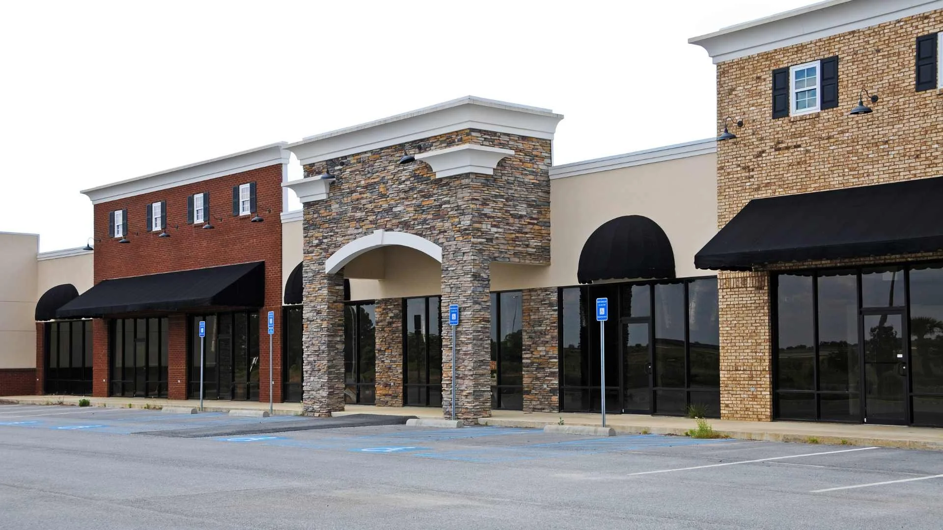 Vacant retail strip mall with various storefront designs and empty parking lot.