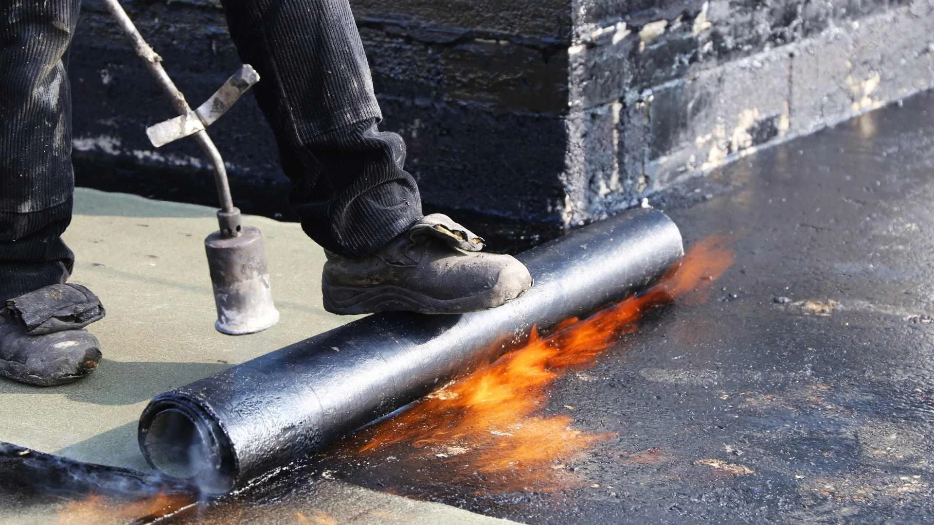 a roofer using a blowtorch for a roof installation