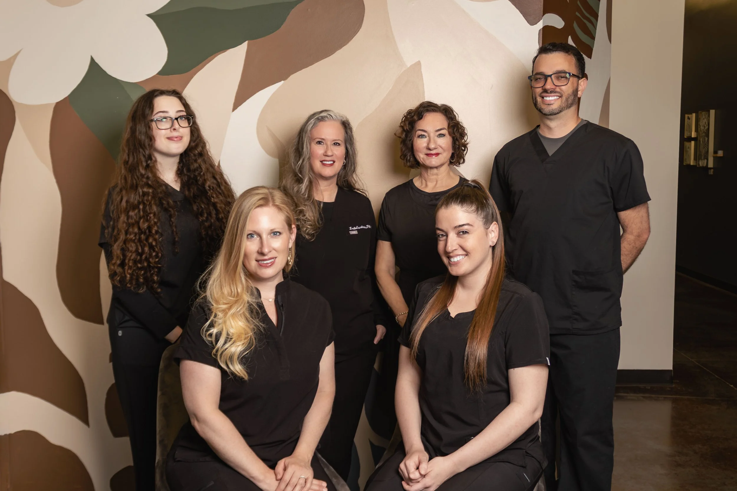 Alma Esthetics team smiling in front of a modern mural.