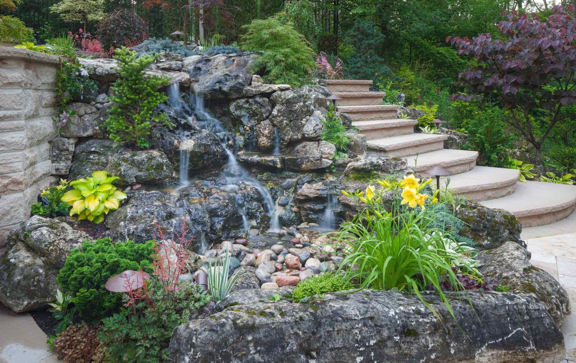 Dundas backyard landscape design with a custom waterfall beside a tiered stone patio.