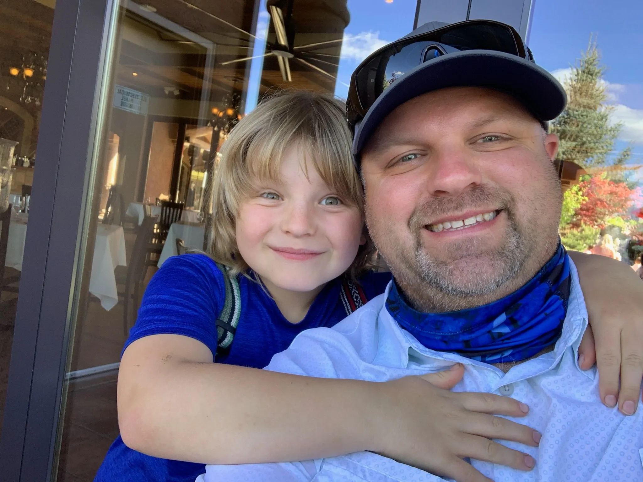 A child and an adult smiling for a selfie outdoors with a restaurant in the background.