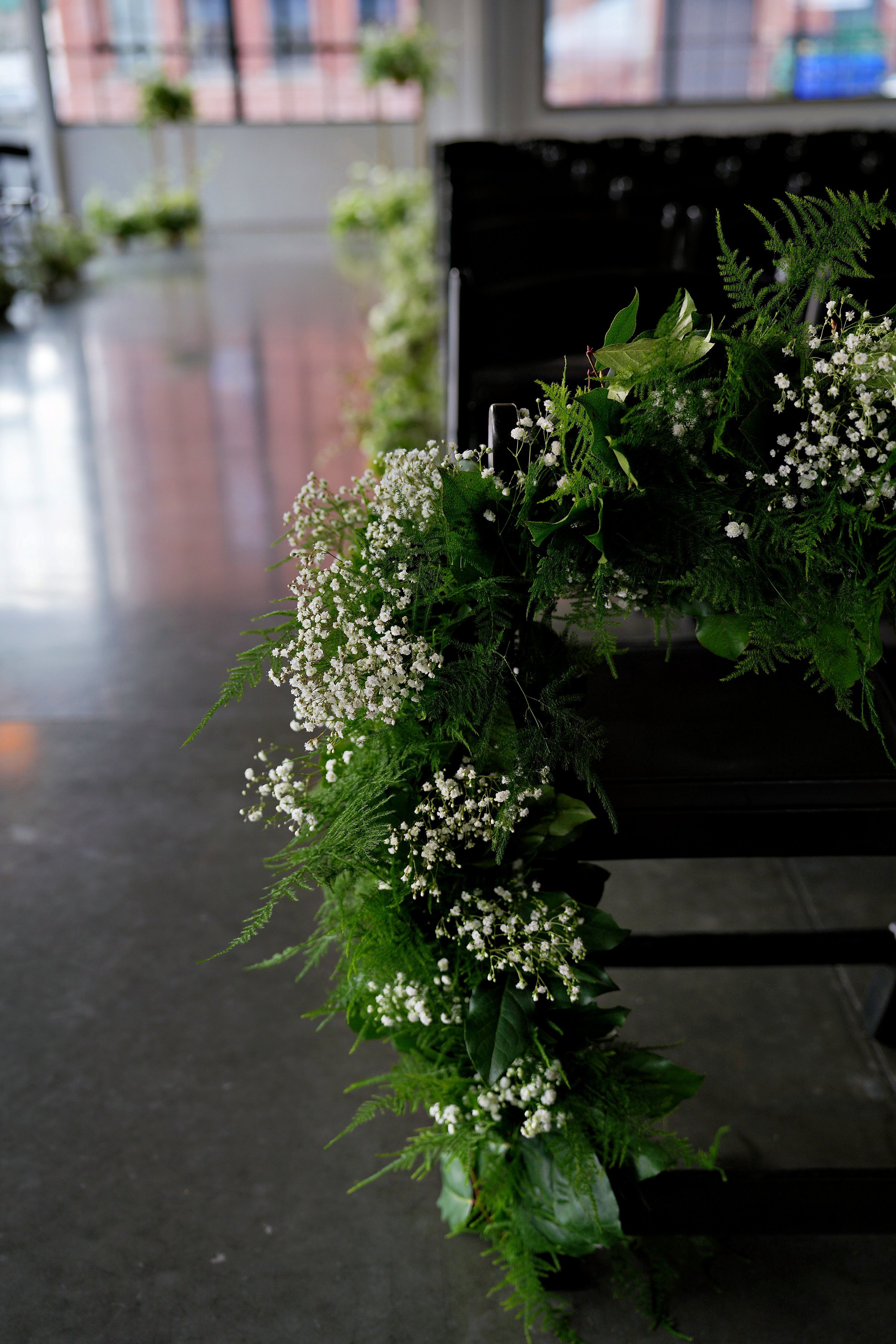 Close-up of lush aisle marker florals featuring baby’s breath and fresh greenery lining a modern indoor wedding ceremony space in Portland, Oregon.