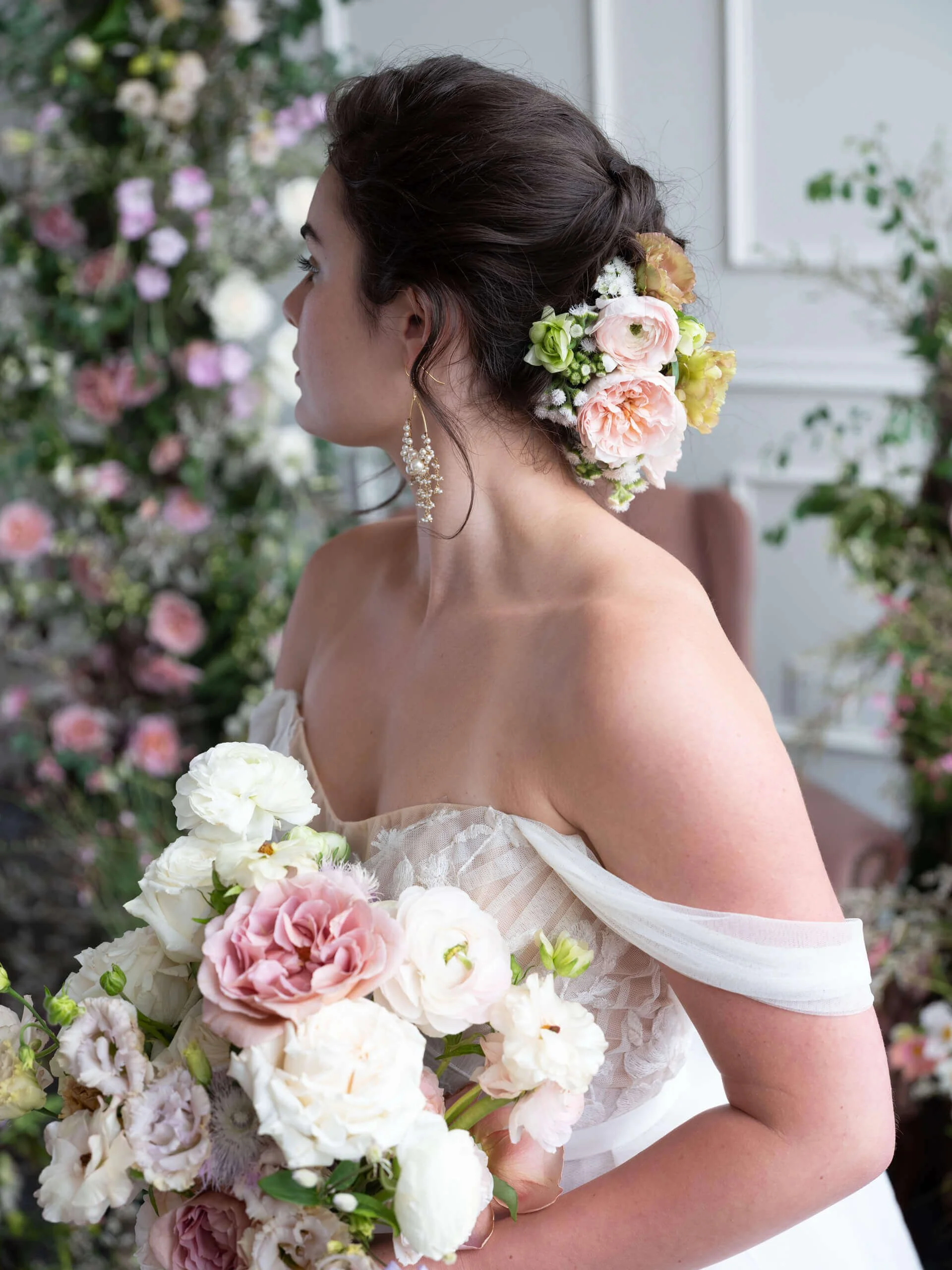 Side profile of a bride with a romantic flower-adorned hairstyle and textured bouquet, styled in a whimsical floral backdrop at Tendue.