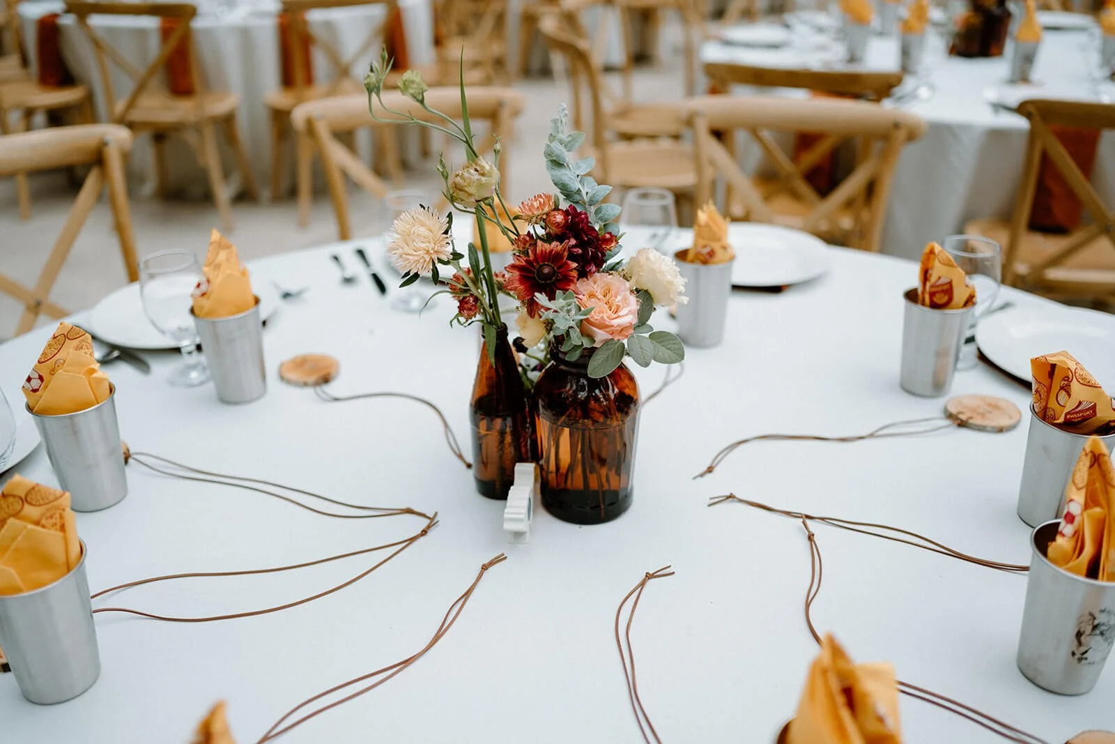 A close-up of a wedding table centerpiece featuring amber glass bud vases with seasonal flowers.