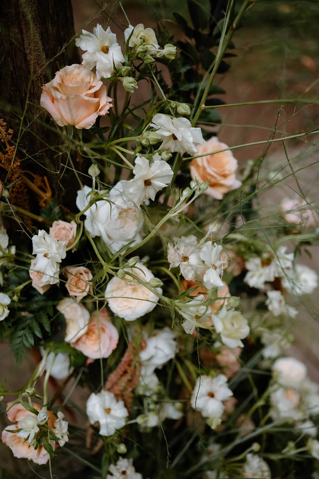 Close-up of a grounded floral arrangement featuring cream, peach, and blush roses mixed with textural greenery.