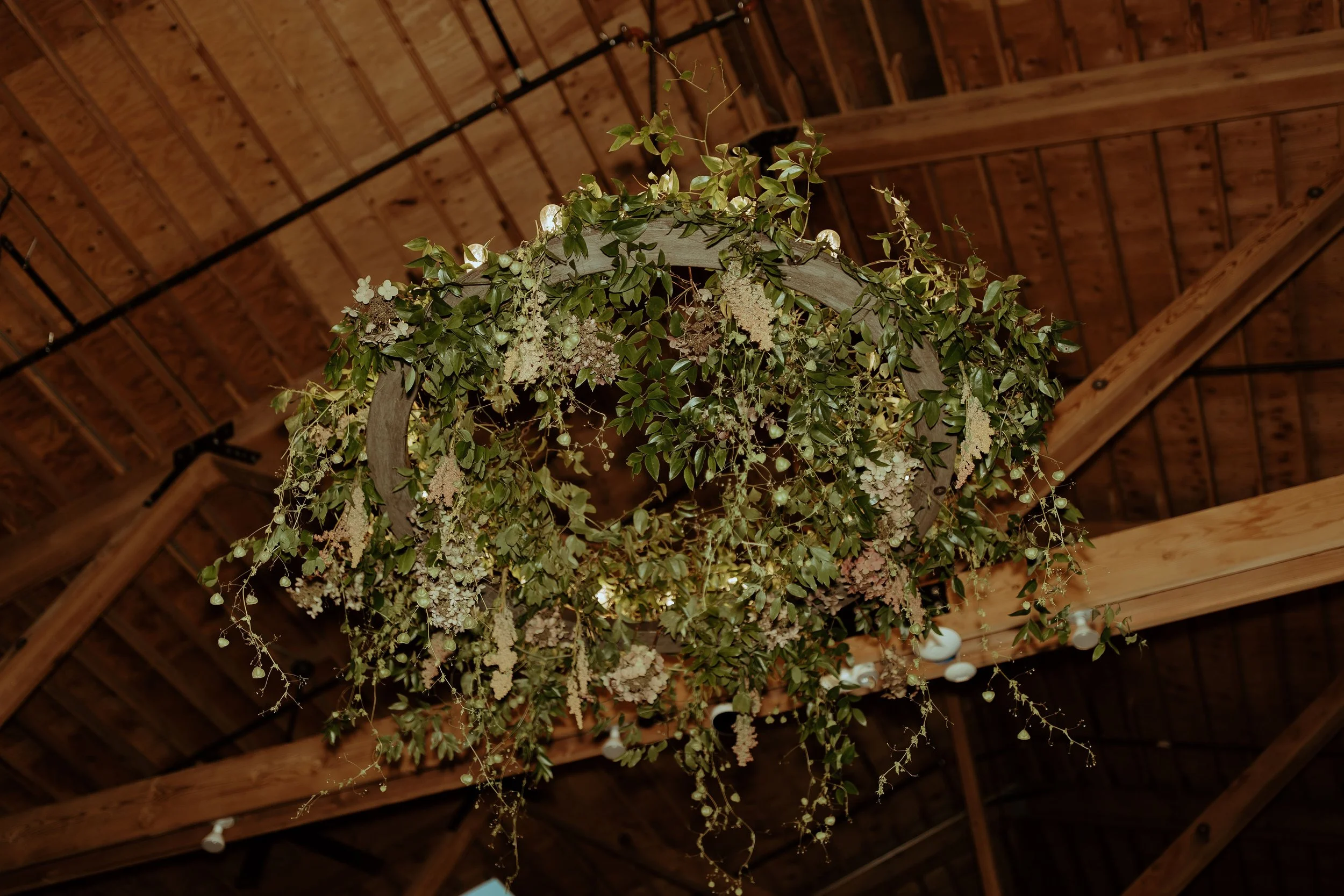 A floral hanging installation suspended above the reception space, covered in locally foraged vines, seasonal greenery, and wildflower-inspired blooms.