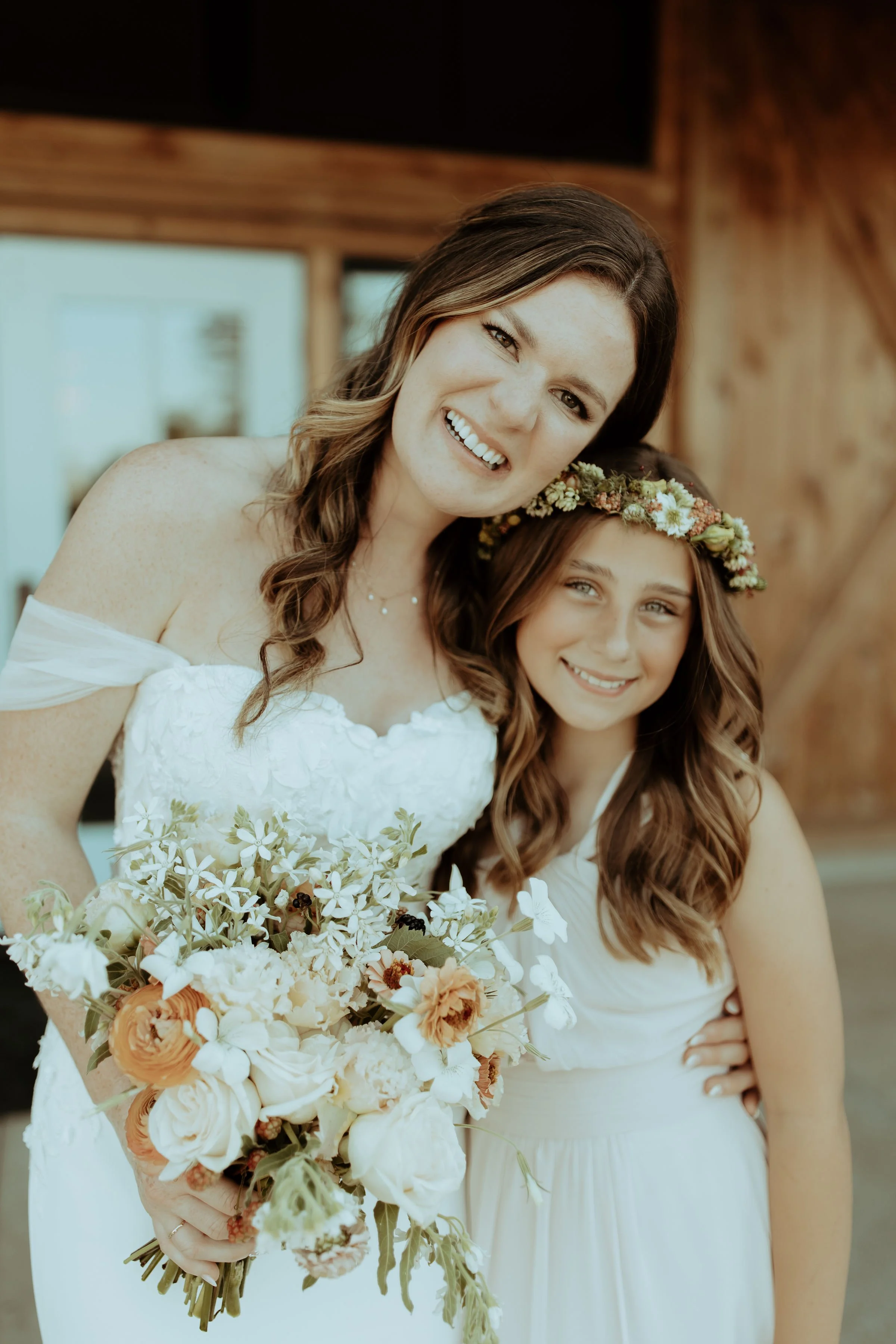 Bride and flower girl wearing a floral crown, smiling outside the barn at Abbey Road Farm wedding venue in wine country.