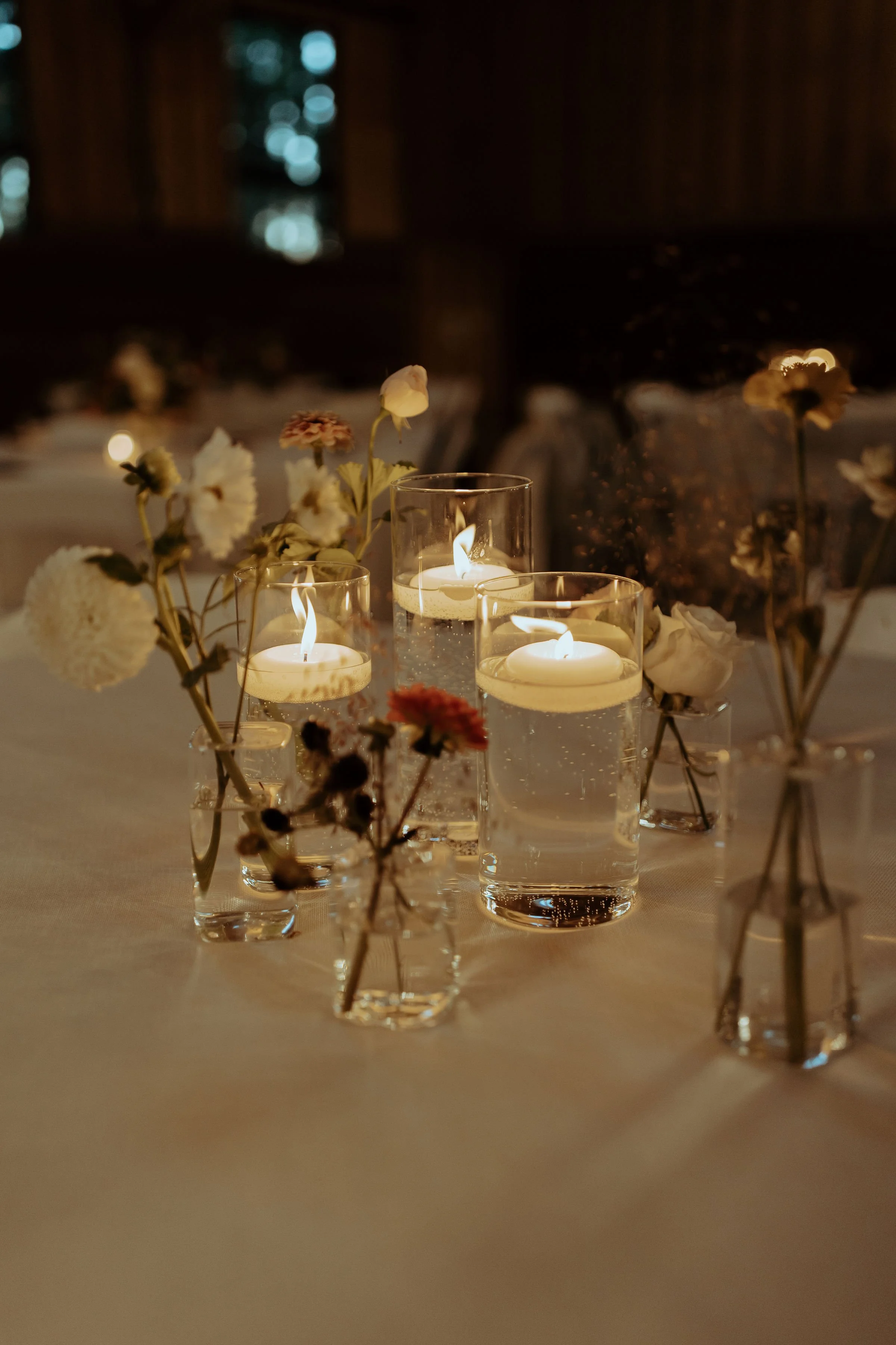 Intimate tablescape filled with floating candlelight and soft accent blooms in neutral tones.