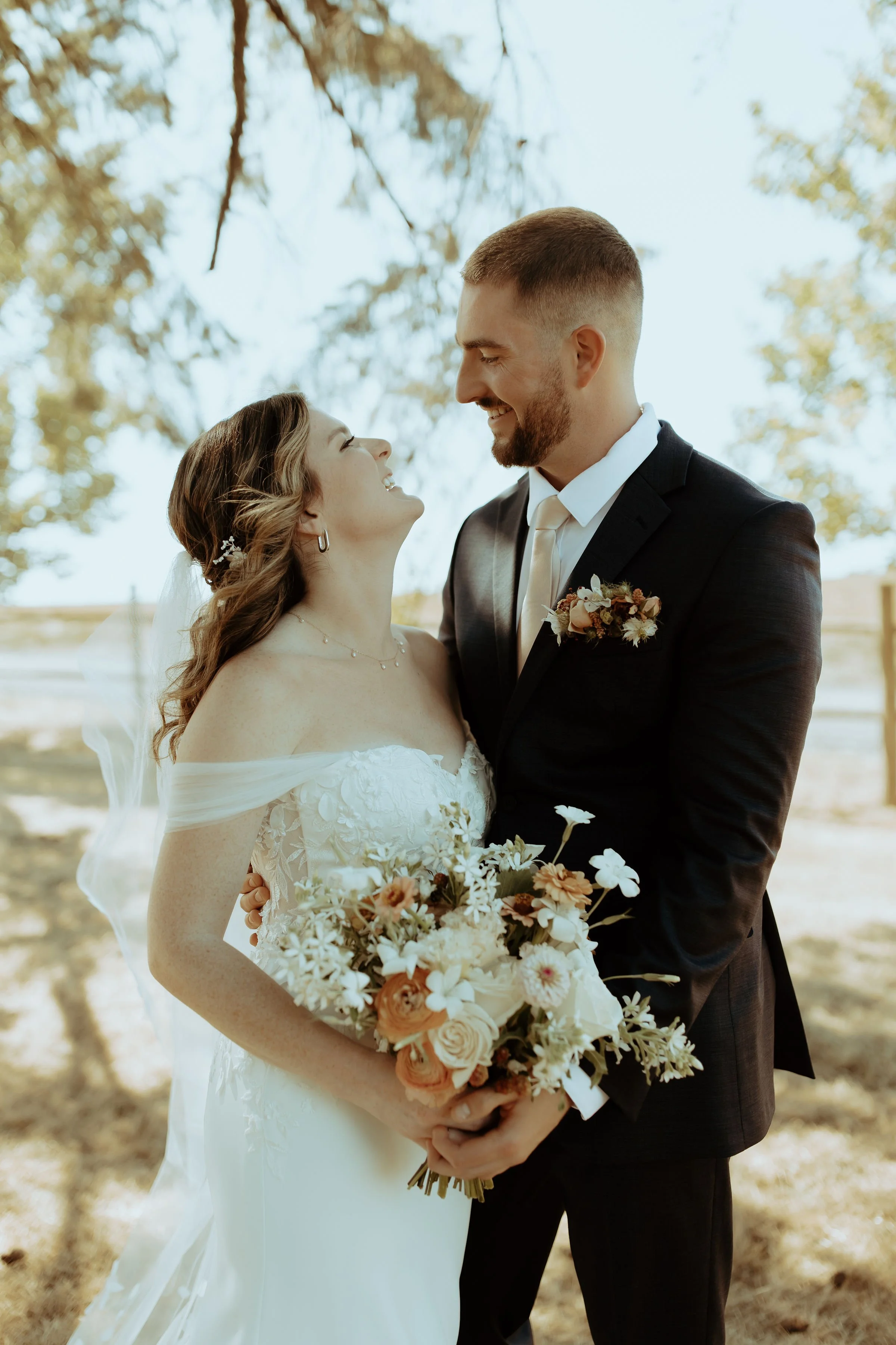 The bride’s bouquet featured homegrown dahlias, zinnias, and roses in soft peach and ivory hues, perfectly complementing her off-the-shoulder lace gown.
