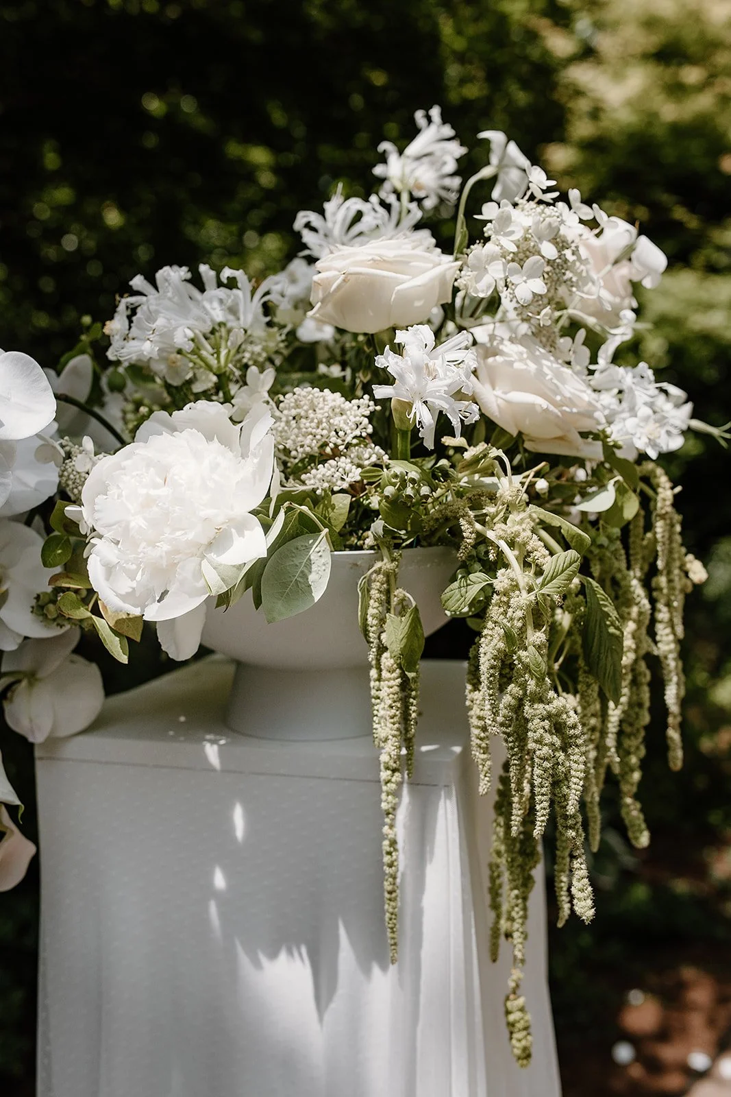 A textural all-white moment from a backyard wedding ceremony in Portland. Featuring locally sourced blooms like peonies, roses, nerine, and trailing amaranthus, designed by Roots of Joy with sustainable mechanics.