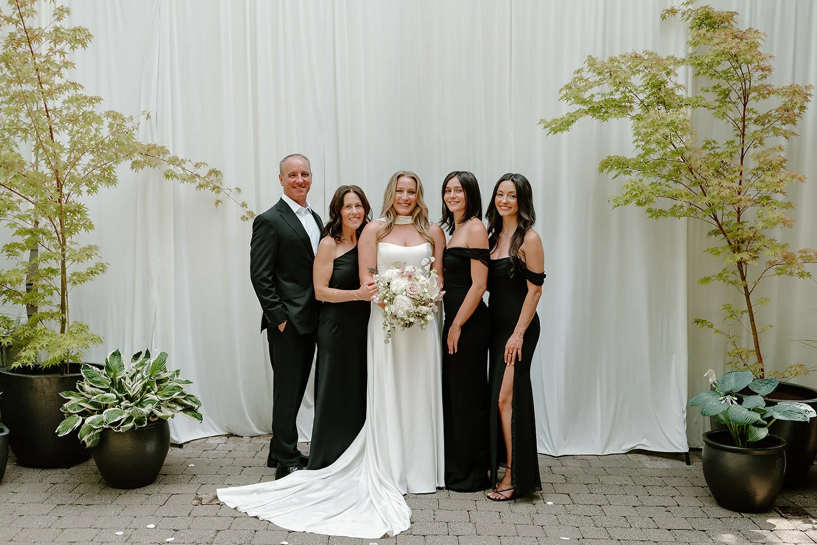 Elegant wedding party portrait in front of a modern white draped backdrop, featuring the bride with family. Floral bouquet with locally grown, seasonal blooms designed by Portland florist Roots of Joy.