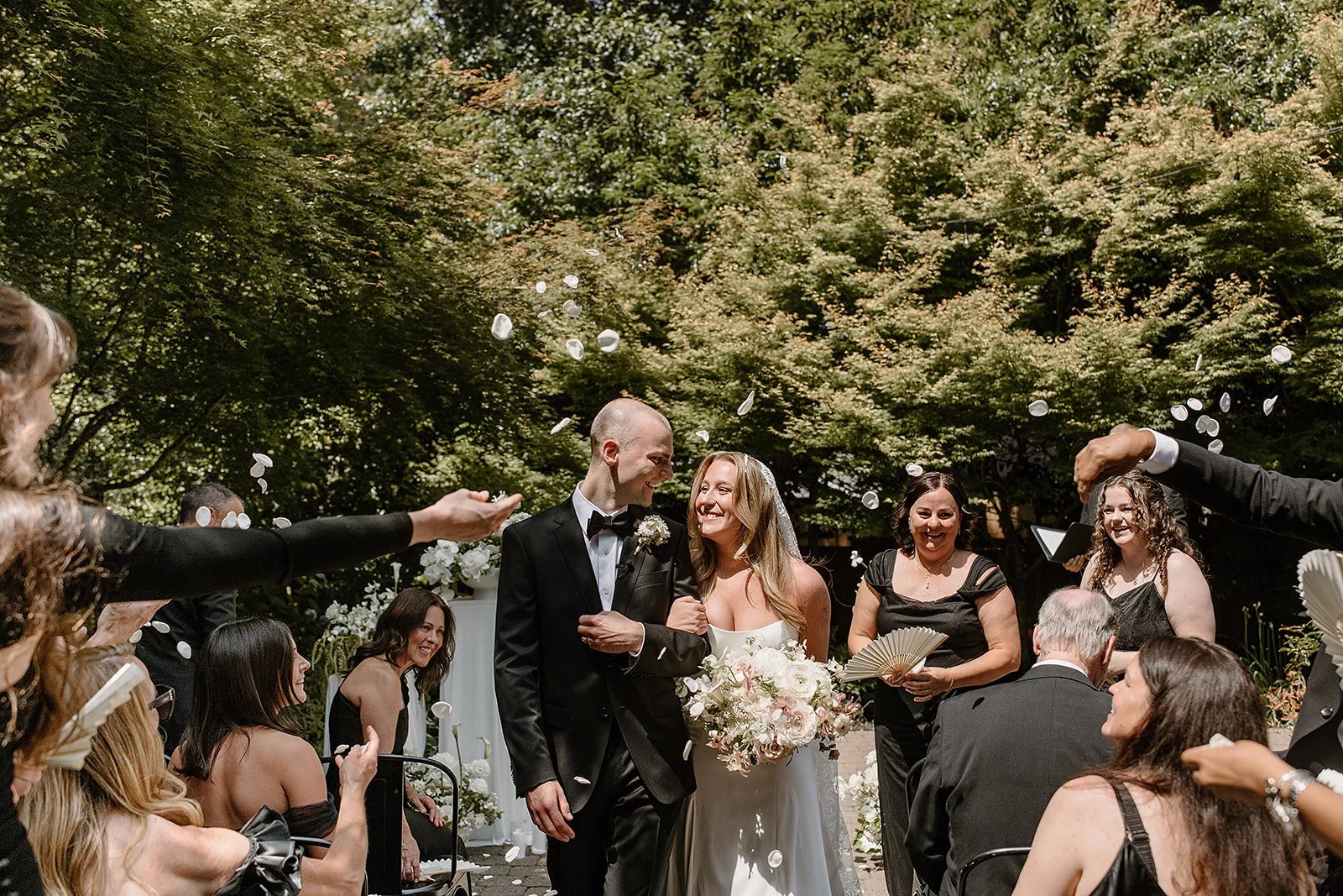 A joyful petal toss moment at a romantic backyard wedding in Portland, Oregon. The bride carries a garden-style bouquet of locally grown, seasonal blooms designed by Roots of Joy.