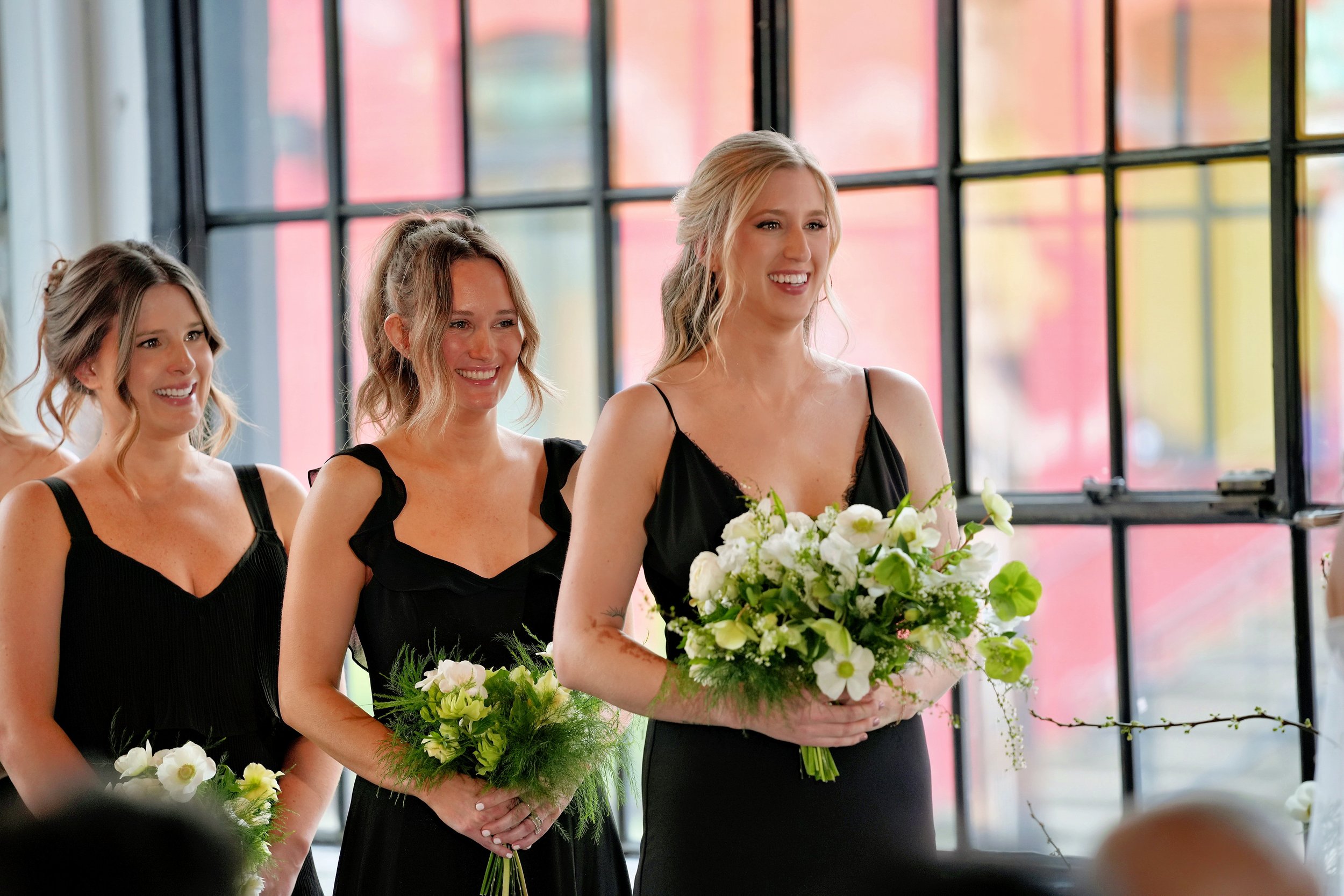 Bridesmaids holding fresh, gathered bouquets of white ranunculus, lisianthus, hellebores, and sweet peas—accented with lacy spirea and soft greenery for a textural, natural look.