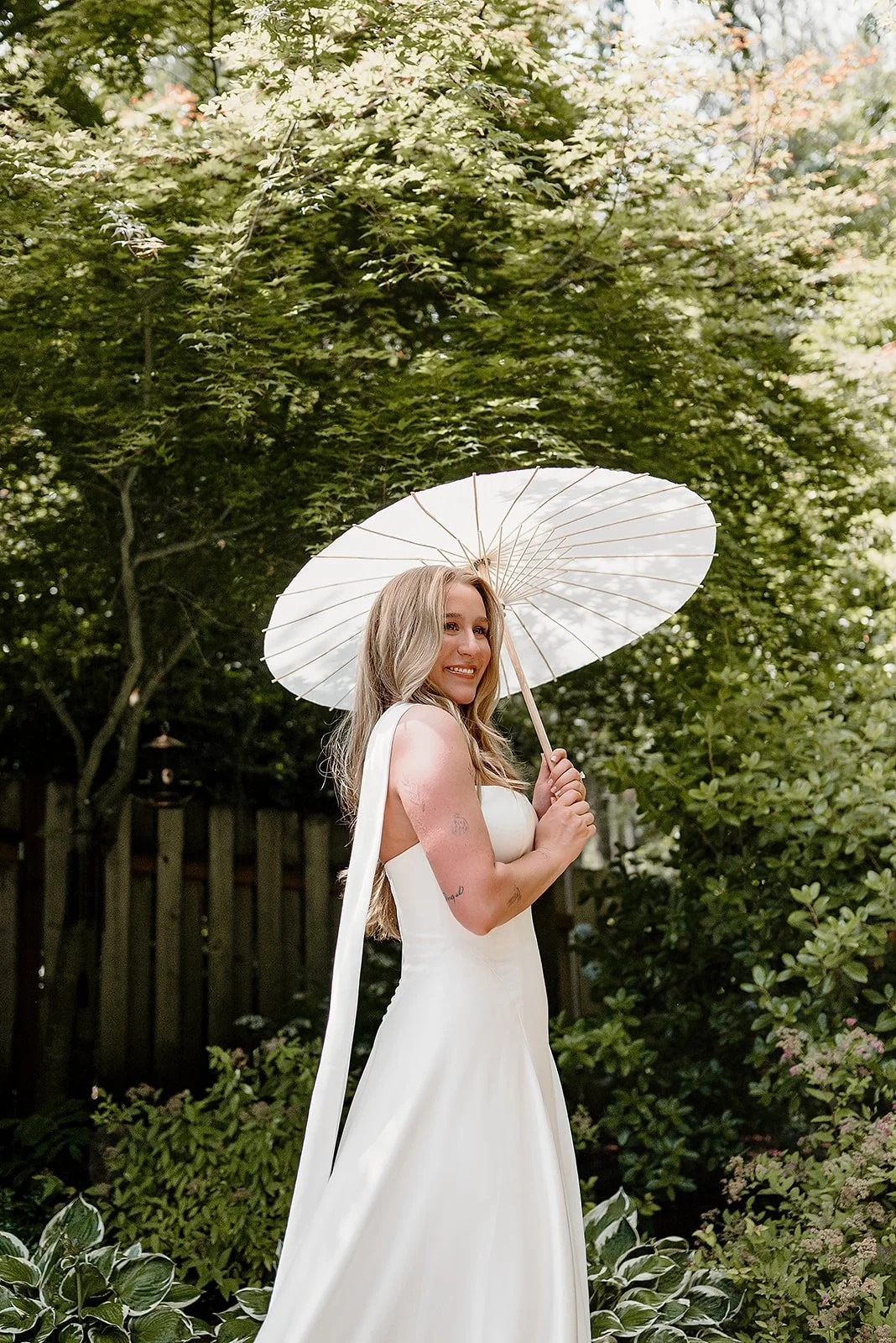 A radiant bride beneath a garden parasol during her elegant backyard wedding in Portland, Oregon. Featuring locally grown flowers and sustainable floral design by Roots of Joy.