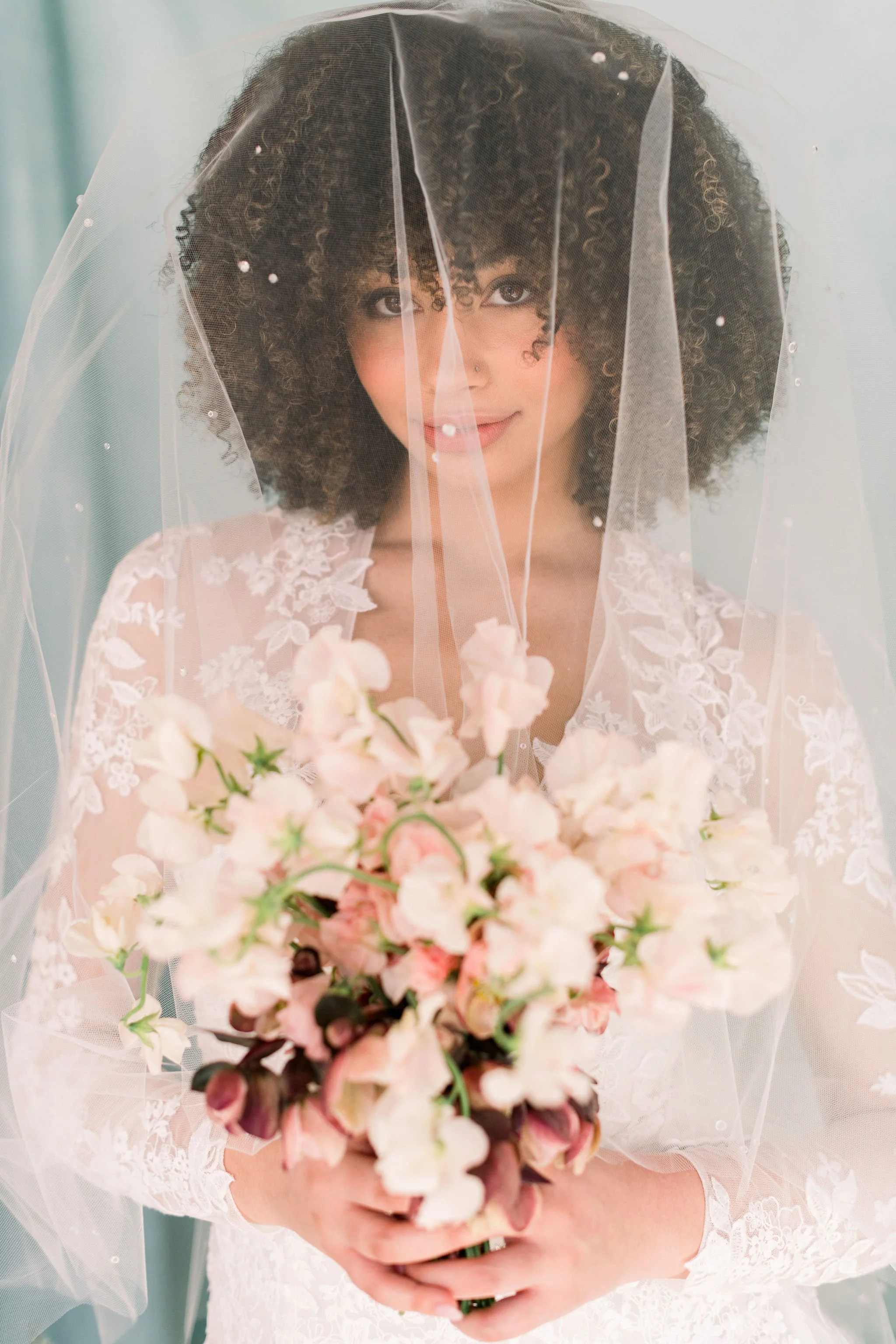 Bride in embroidered lace gown holding a structured bouquet of sweet peas in pink and wine hues by Roots of Joy.