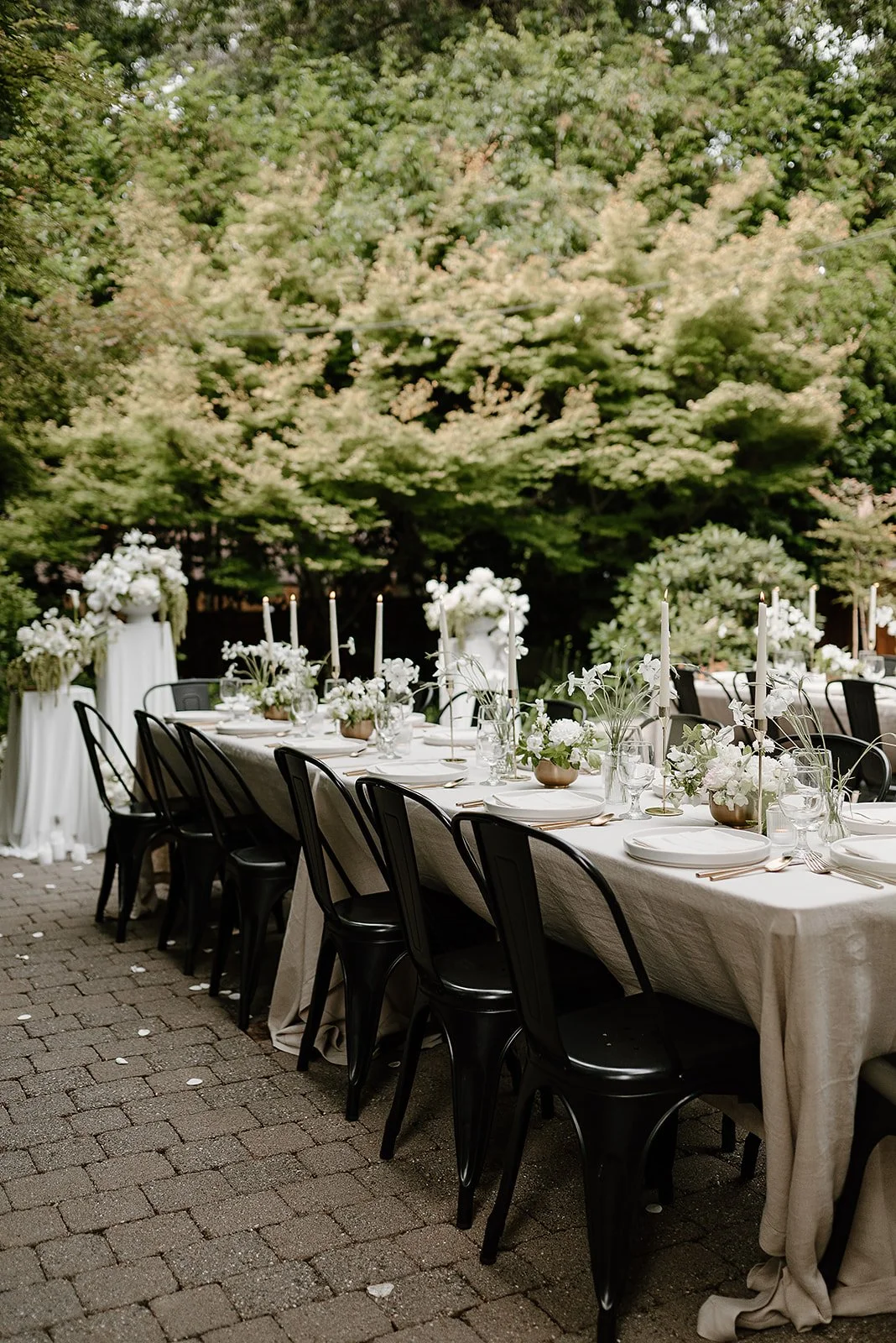 Modern backyard wedding reception table set with neutral linens, white florals, and taper candles in Portland, designed by Roots of Joy.
