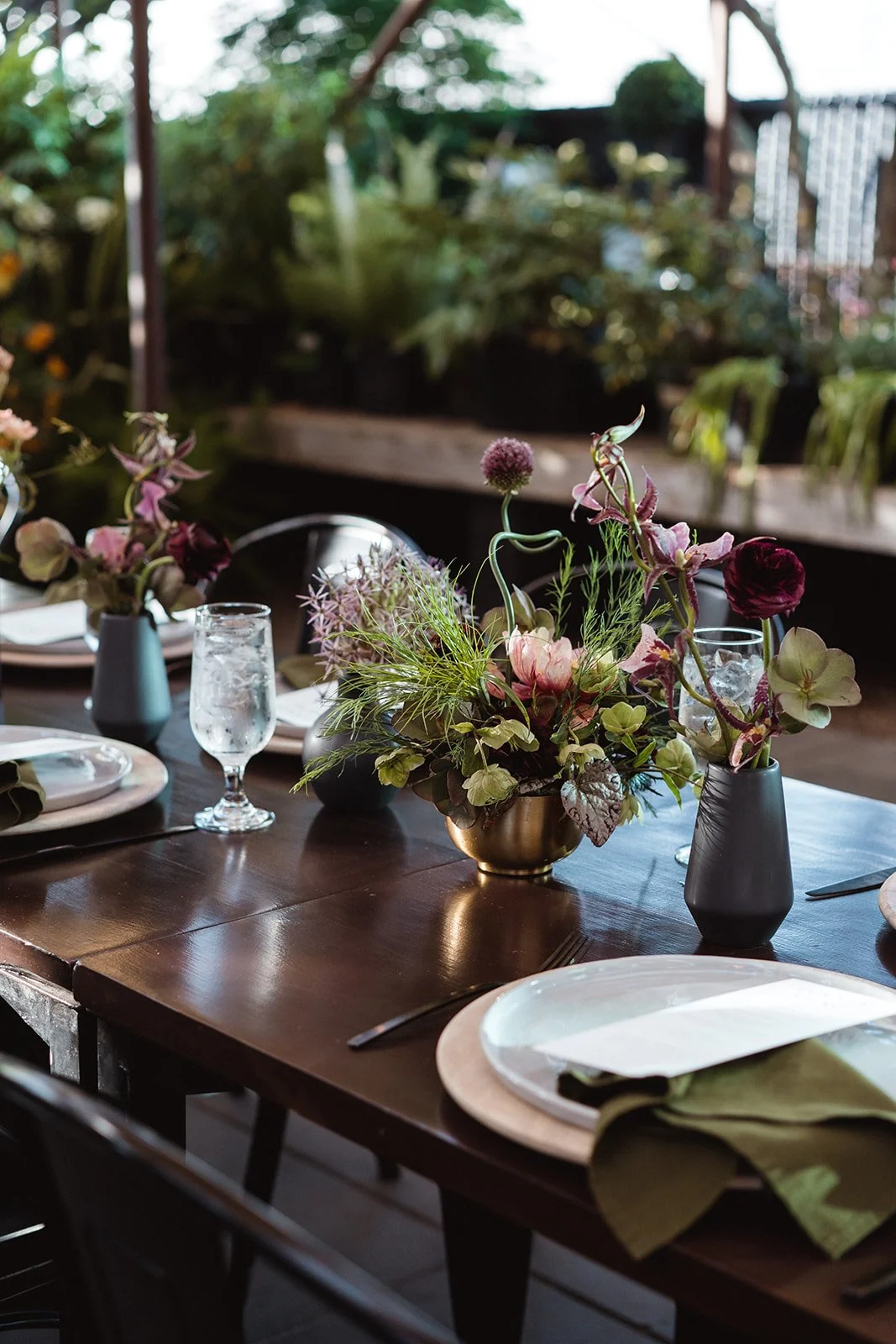View of wedding dinner place settings, menus, and bud vase florals styled with delicate greenery and seasonal blooms.