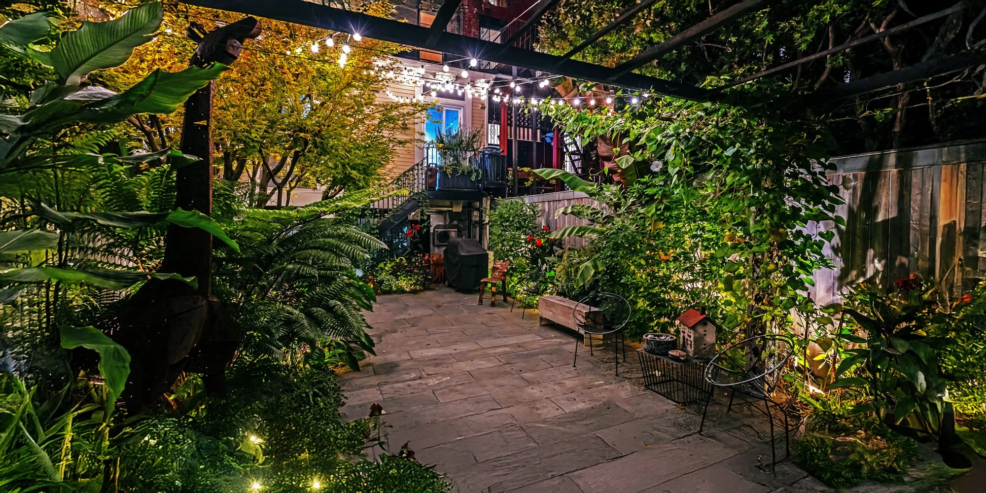 backyard garden in Brooklyn  at dusk with modern lighting, lush plantings, and outdoor seating