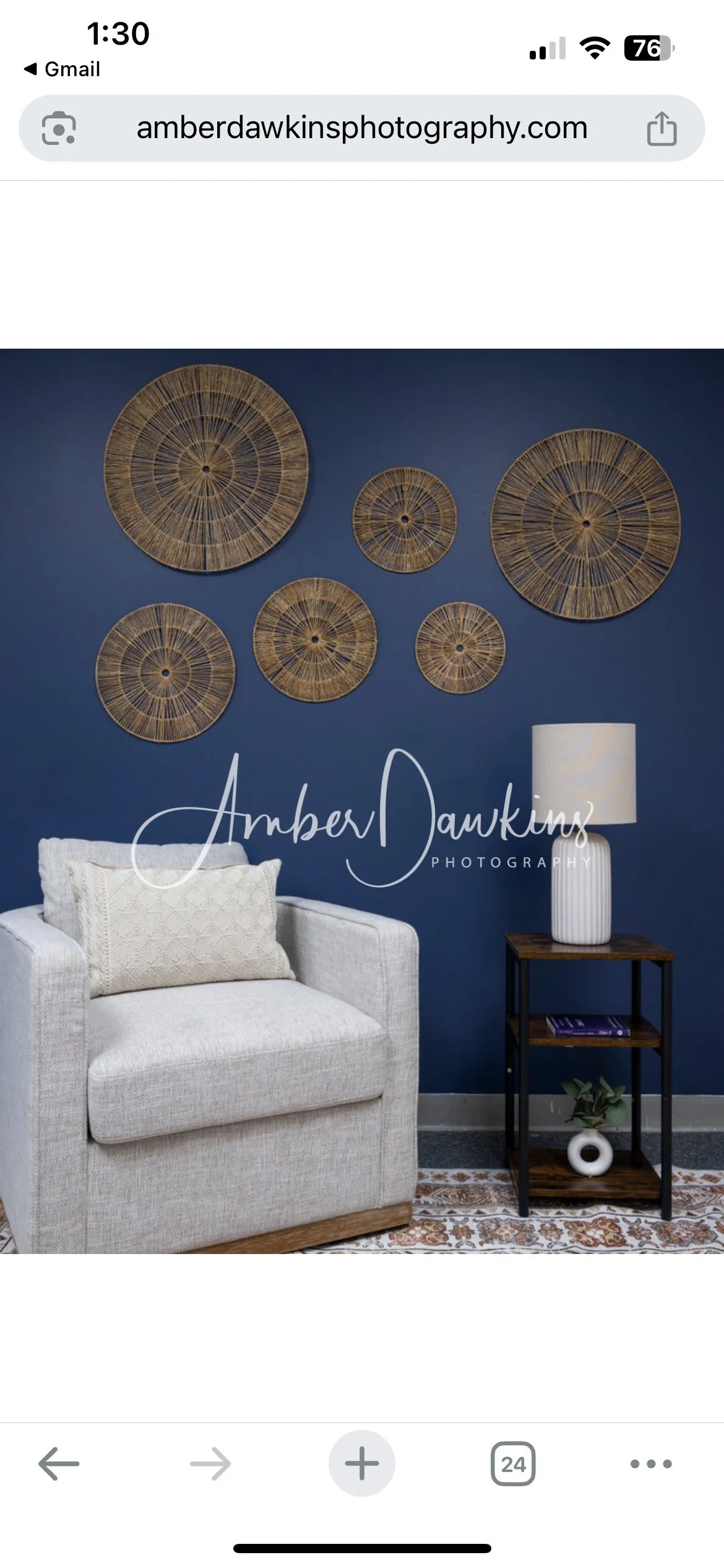 Interior living room with dark blue wall decorated with six round wicker wall hangings, a white armchair with a beige cushion, a small wooden table with a white lamp, a book, and a small potted plant, on a patterned rug.