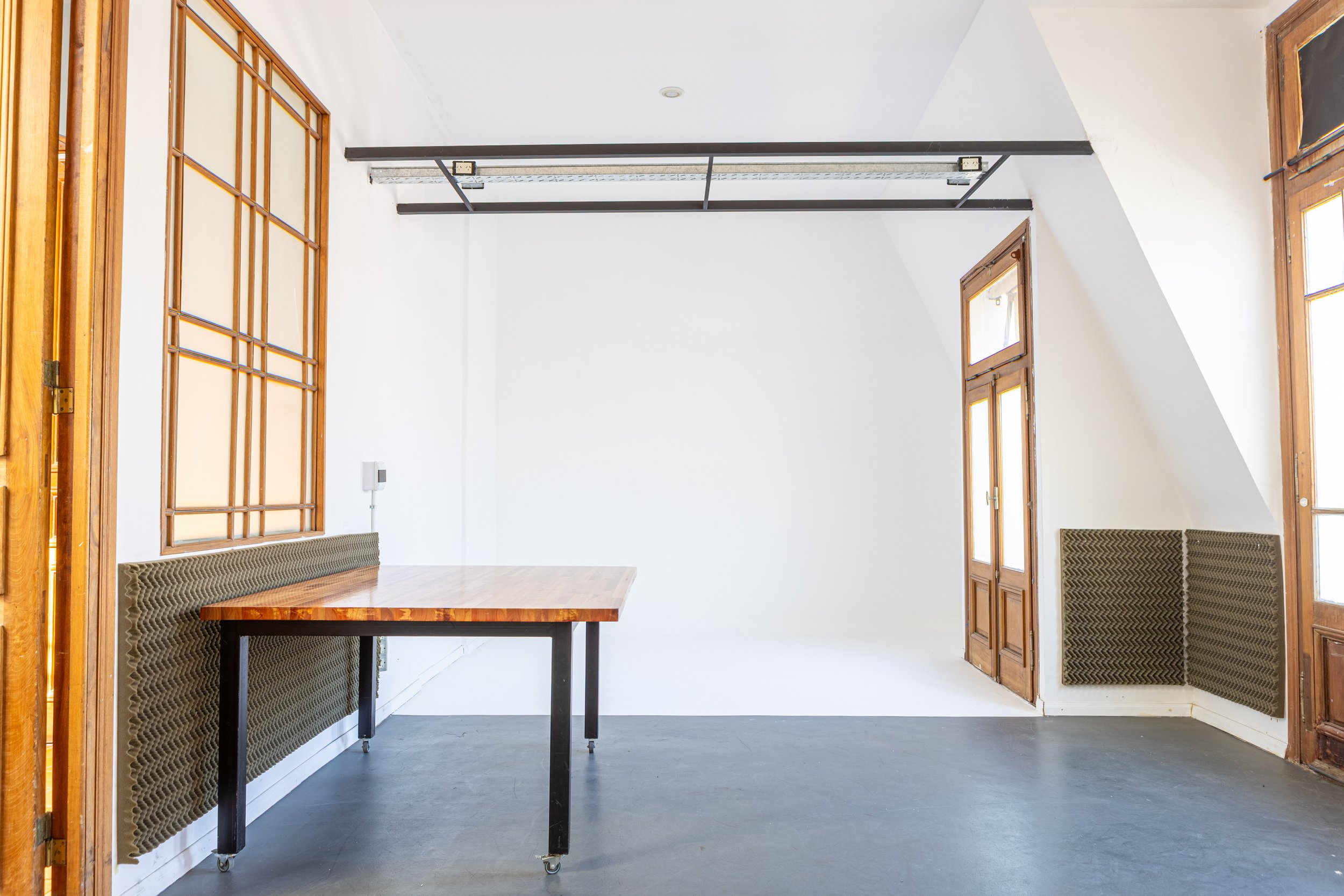 Habitación con paredes rosa, espejo con luces, taburete negro, y silla blanca de madera en el suelo de madera clara.