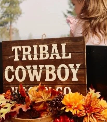 Tribal Cowboy Wagon Co. wooden sign decorated with fall leaves and flowers, with a woman visible in the background