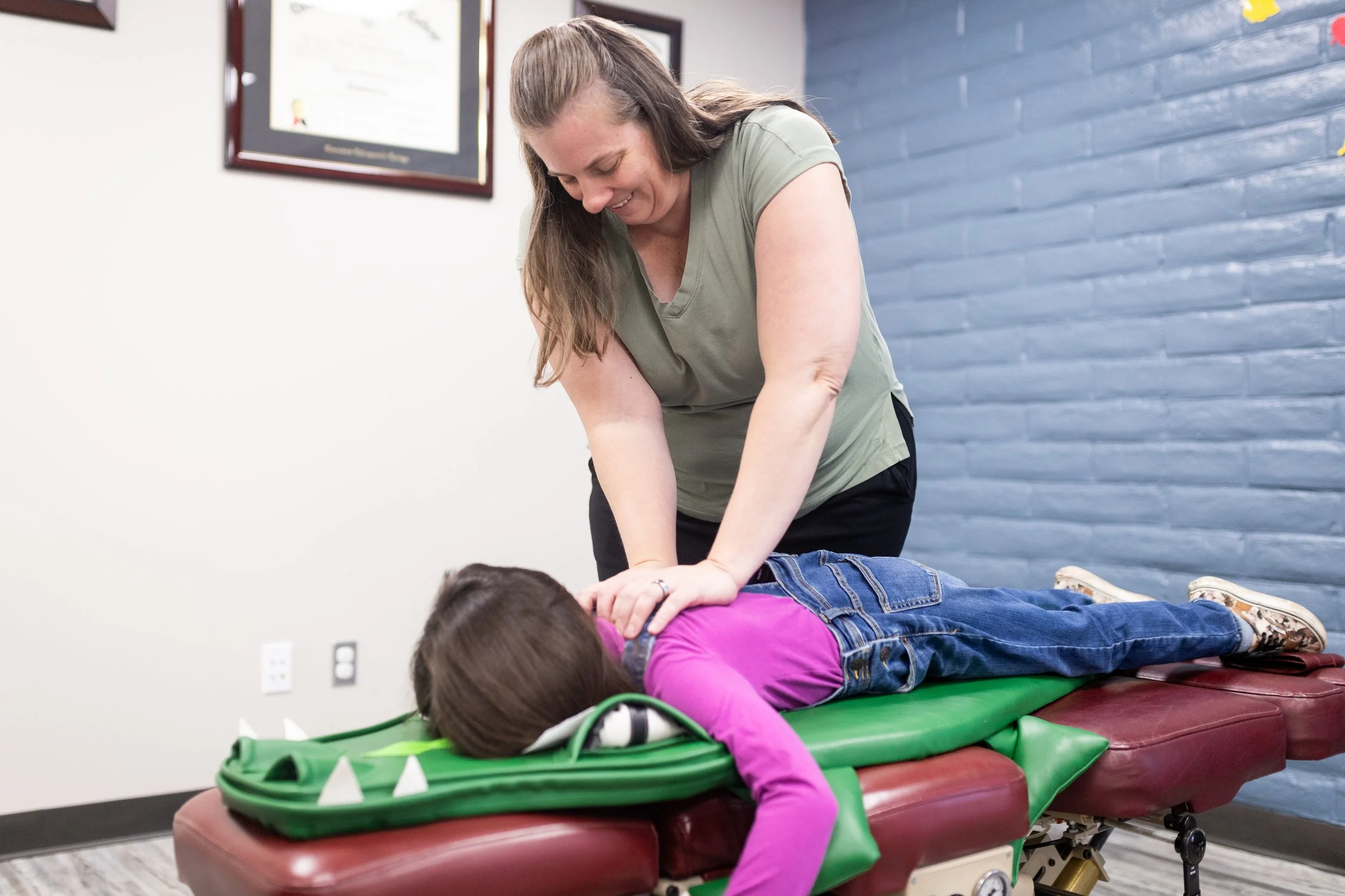 A woman receives chiropractic care from a chiropractor who is adjusting her back while lying face down on a treatment table in a clinic.