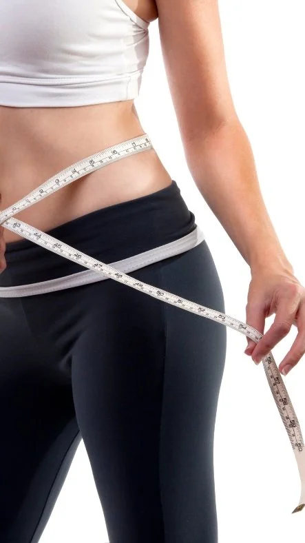 Close-up of a woman's waist and hand measuring her waistline with a tape measure, wearing athletic clothing.
