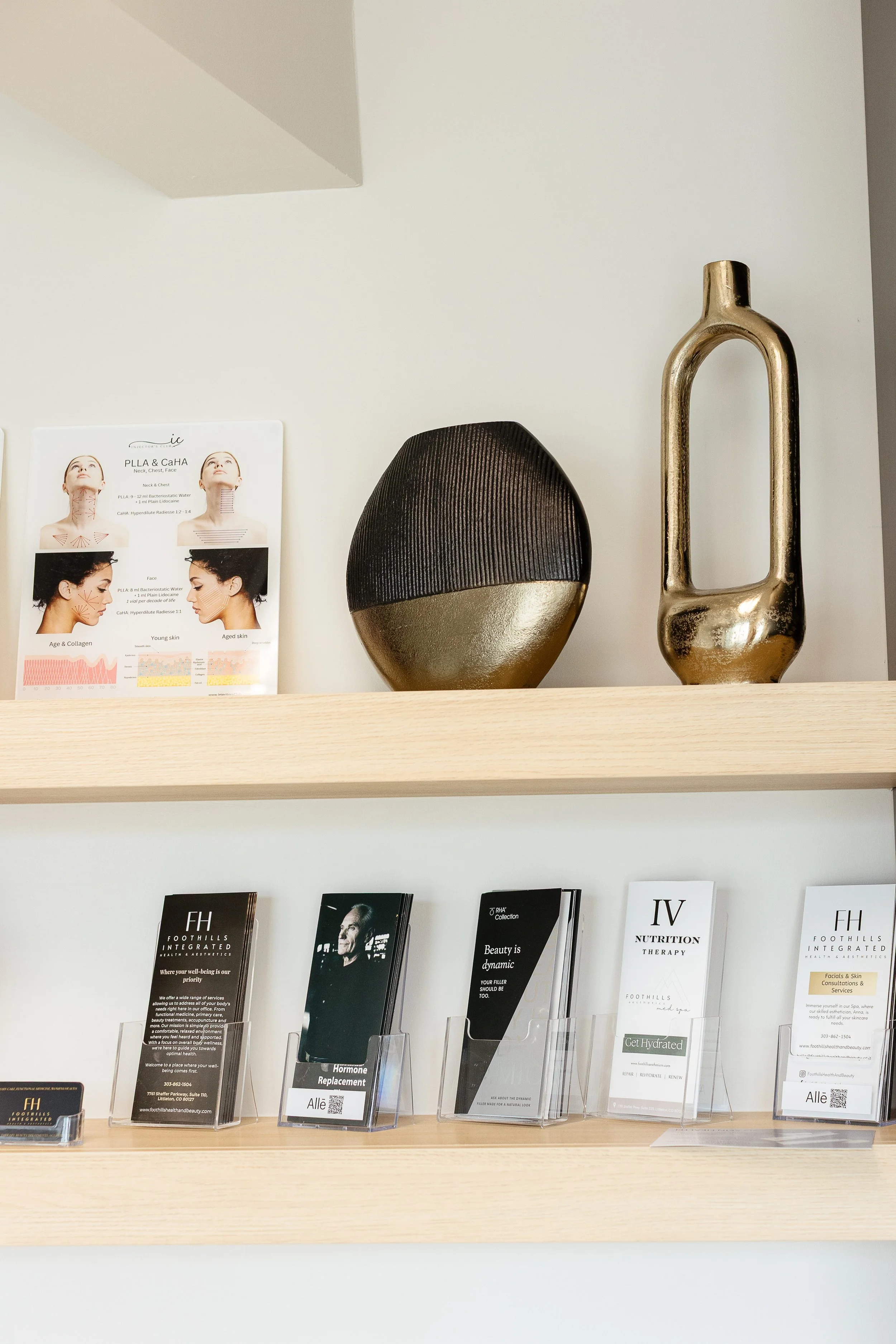 Decorative objects and pamphlets on wooden shelves in a modern waiting area, including a black and gold rounded sculpture, a tall gold sculpture, and informational brochures about health and beauty services.