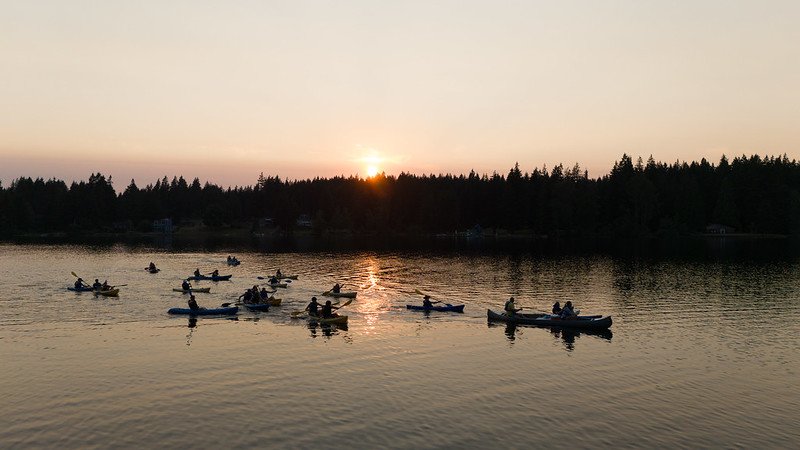 Group of kayakers on a lake during sunset with a tree-lined horizon.