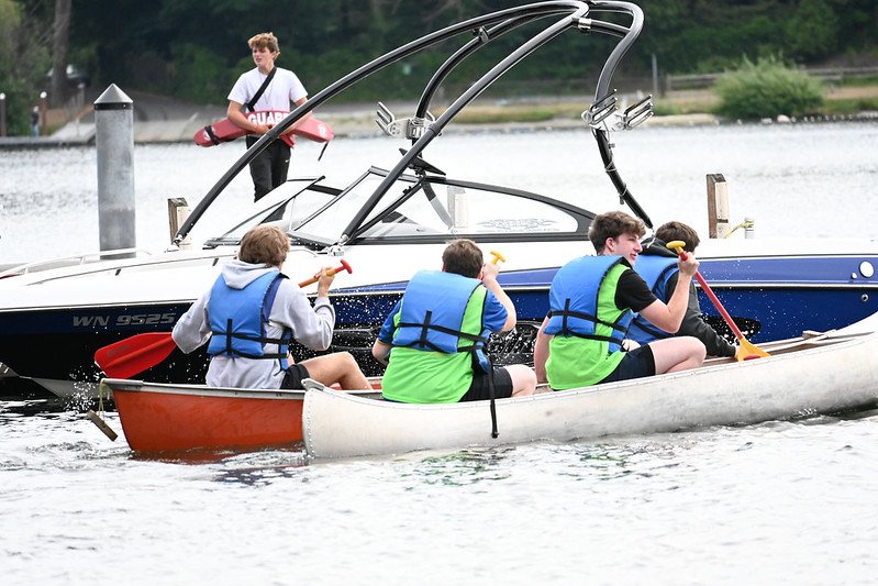 Group of people in blue life jackets canoeing near a motorboat on a lake.